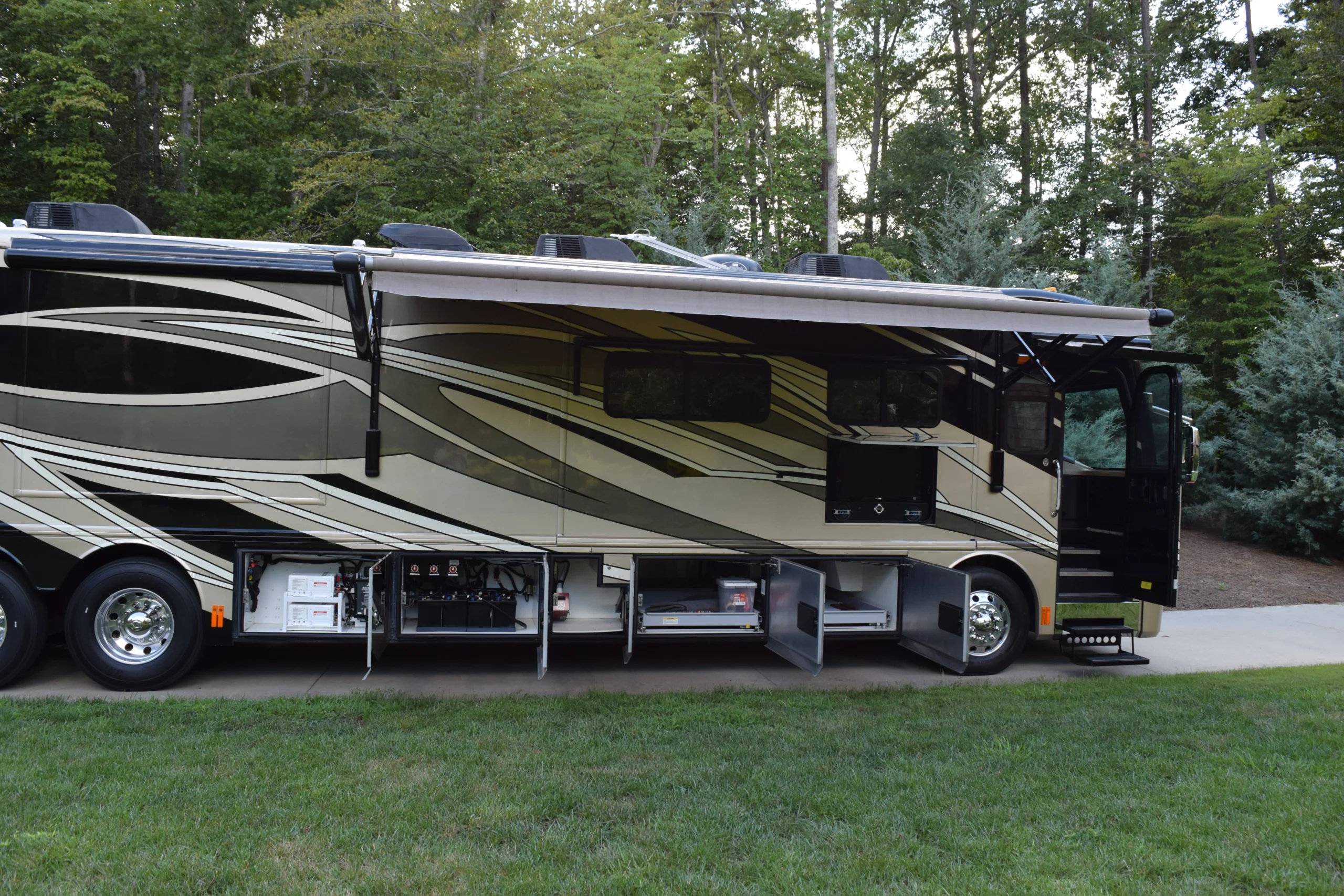 DSC_0355 Luxury motorcoach with open storage compartments in a wooded area, showcasing sleek design and spacious interior access.