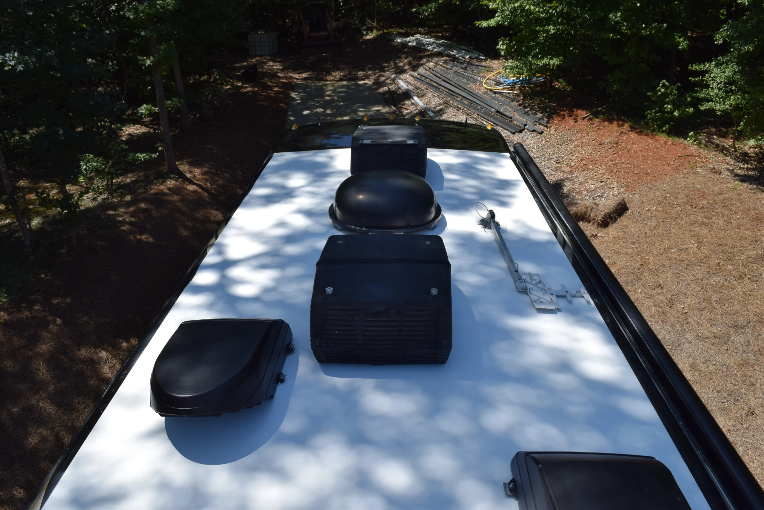 DSC_0359 RV roof with several vents and air conditioning units, parked near trees. Motorcoach and RVs setting.
