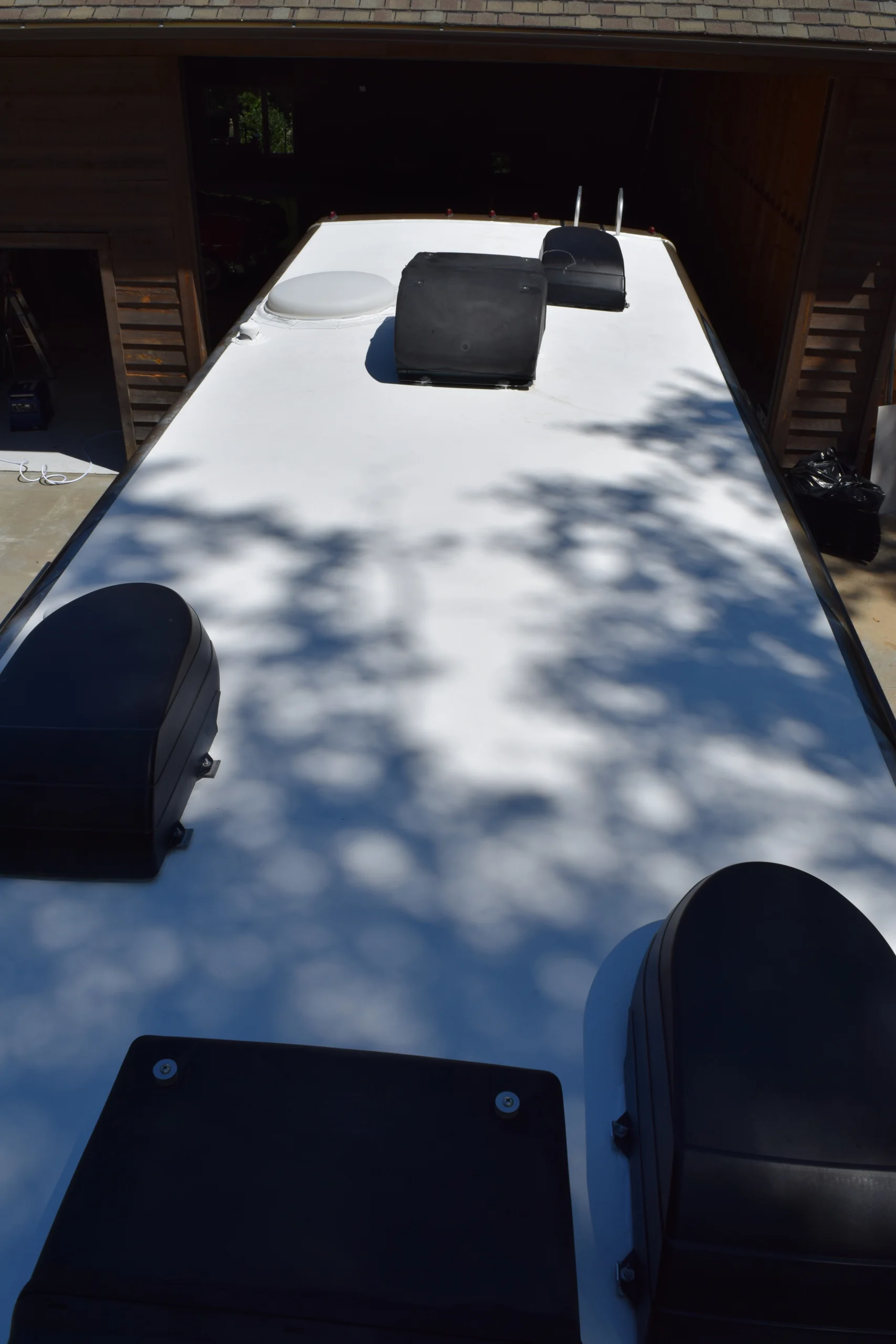 DSC_0361 White roof of a motorcoach with black vents and air conditioning units, dappled with tree shadows.