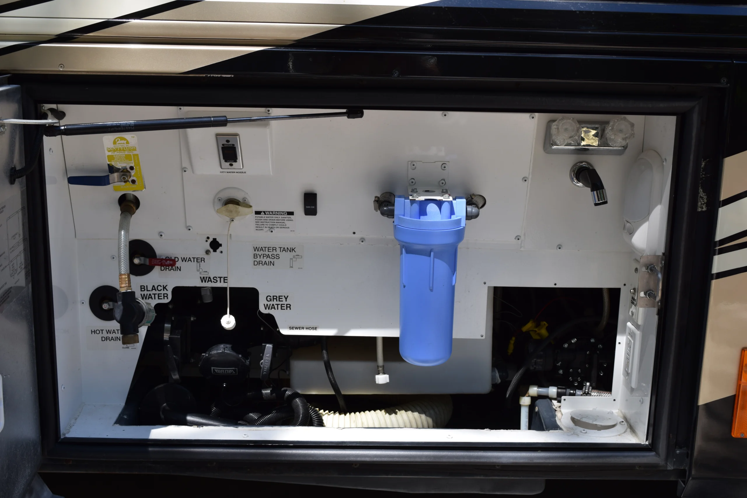 DSC_0362 Interior of motorcoach RV's utility compartment with water filtration system, labeled valves for black and grey water, and various drains.