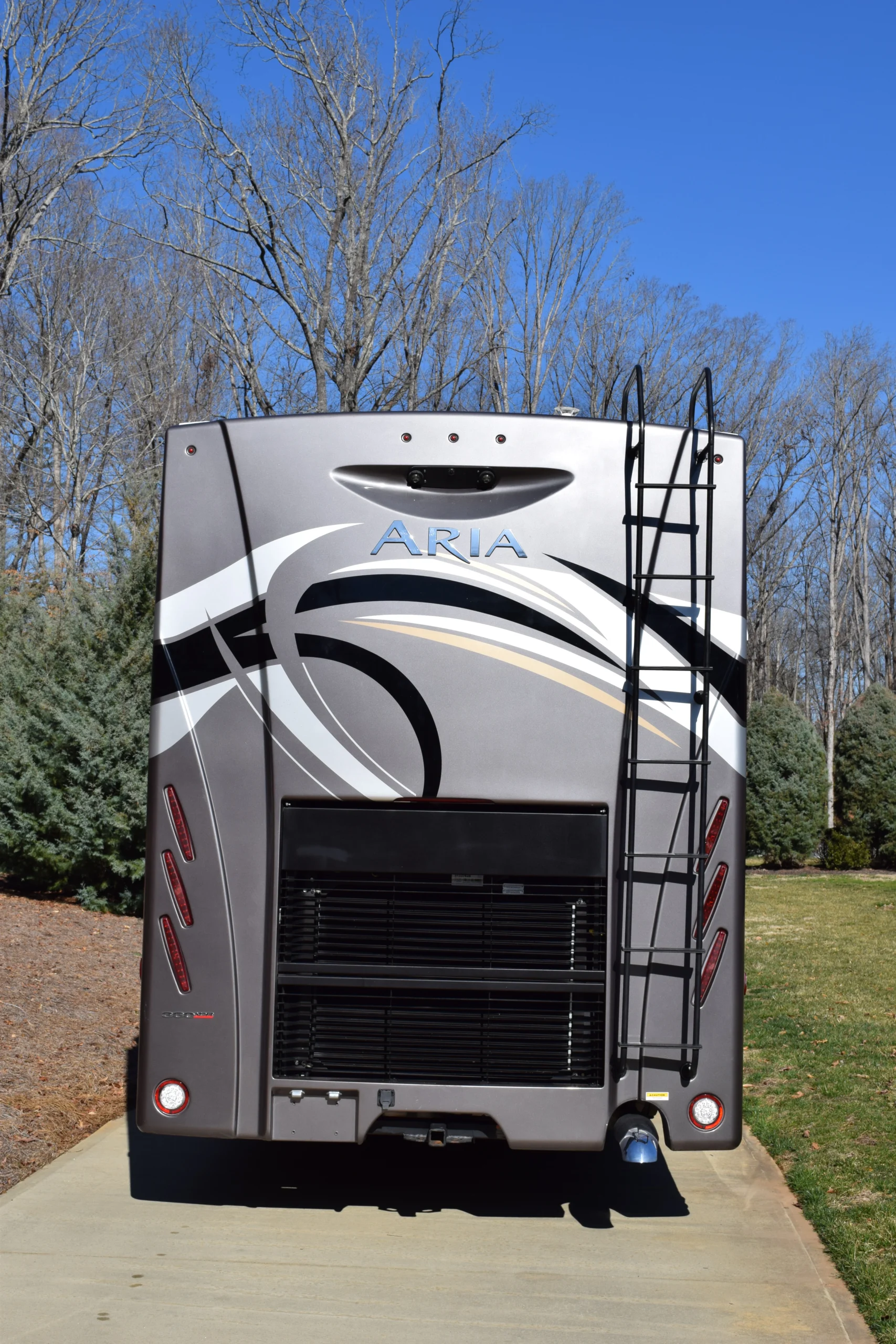 DSC_0375 Rear view of a Motorcoach and RVs unit on a driveway, showcasing a ladder and sleek design against a clear blue sky.