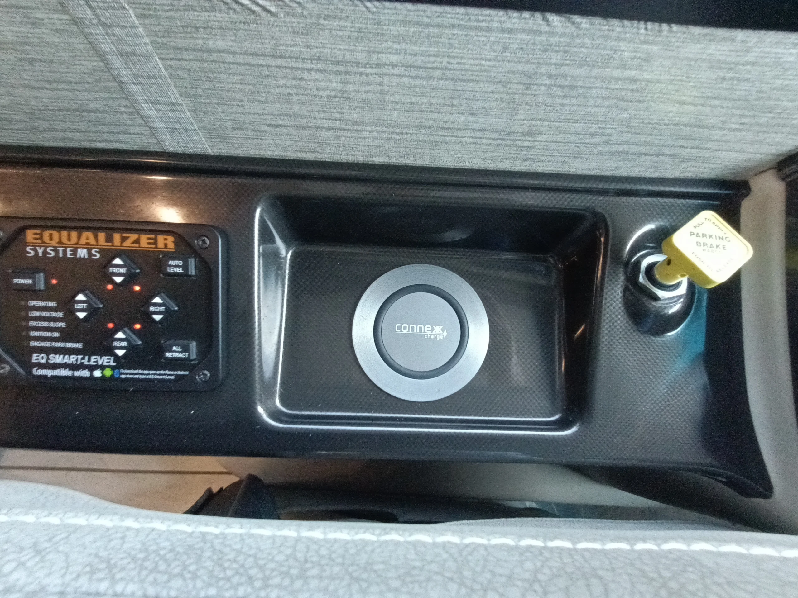 IMG_20260611_190537_287 Dashboard control panel in a motorcoach, featuring EQ Smart-Level system, Connex charger, and parking brake knob.