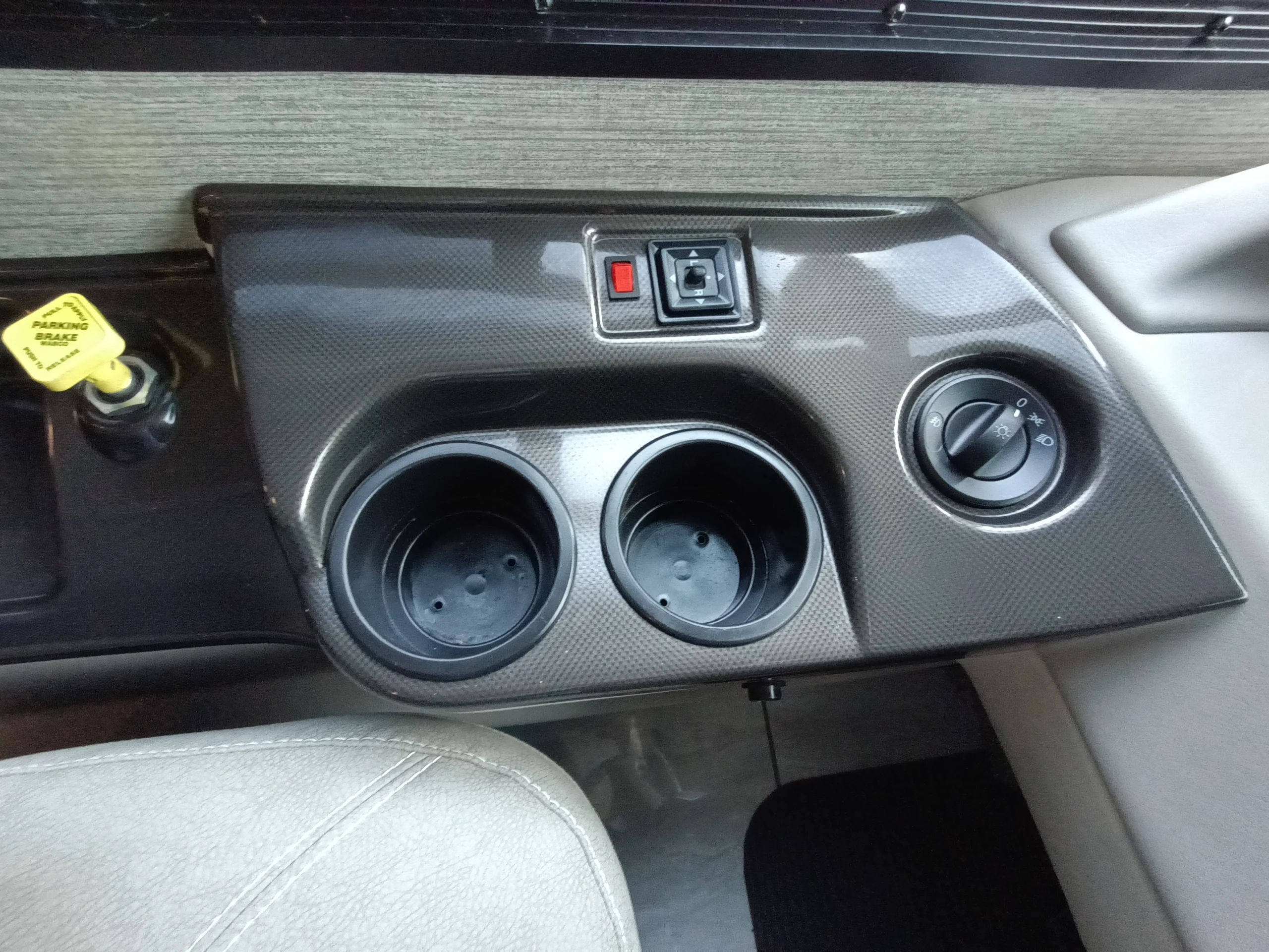 IMG_20260611_190540_694 Dashboard section featuring a parking brake release, dual cup holders, and headlight controls in a Motorcoach and RVs interior.