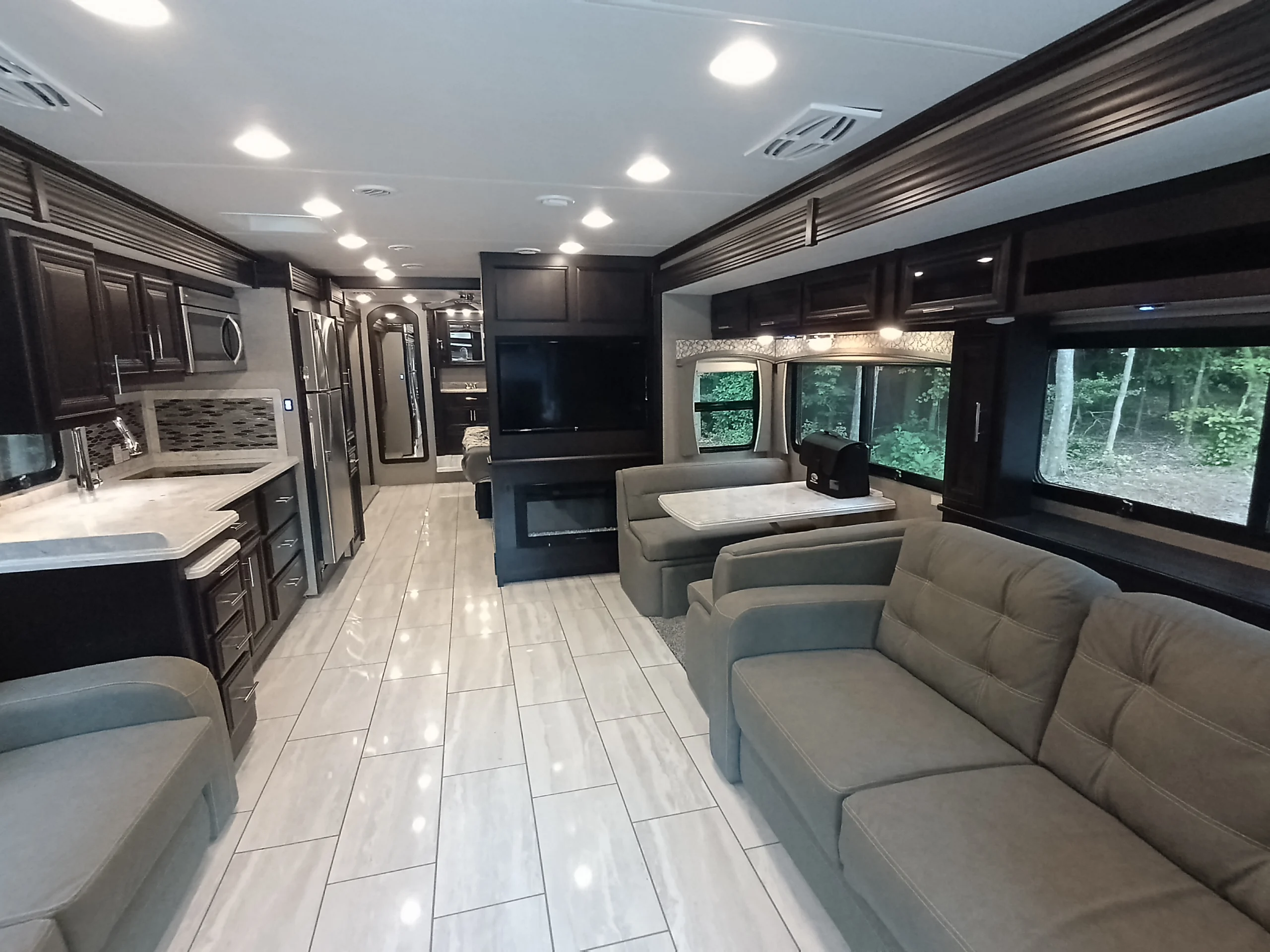 IMG_20260611_190709_701 Luxurious motorcoach interior featuring modern kitchen, spacious seating, large windows, and an entertainment area with a fireplace.