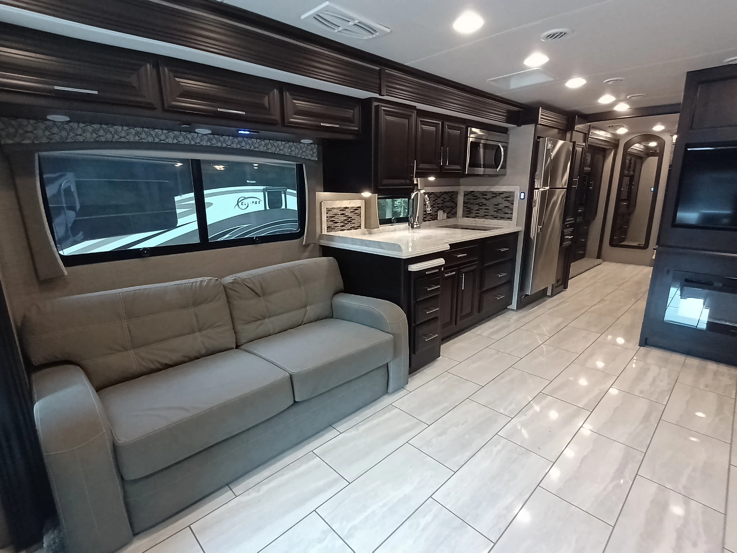 IMG_20260611_190721_888 Luxurious Motorcoach and Rvs interior with brown cabinets, sofa, stainless steel appliances, marble countertops, and a polished tile floor.