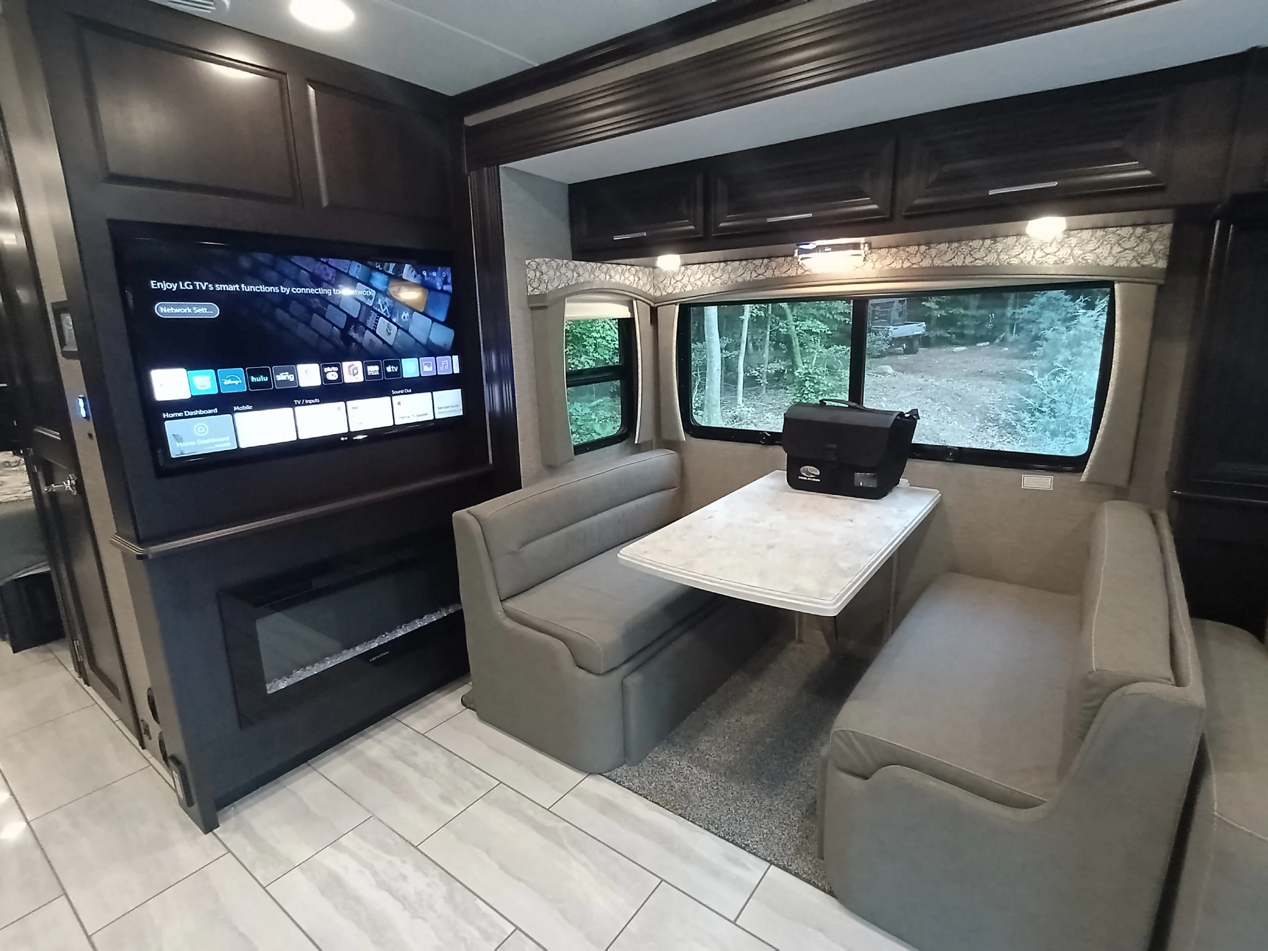 IMG_20260611_191003_435 Luxurious motorcoach interior with a cozy dining area, large window view, mounted TV, and sleek fireplace.