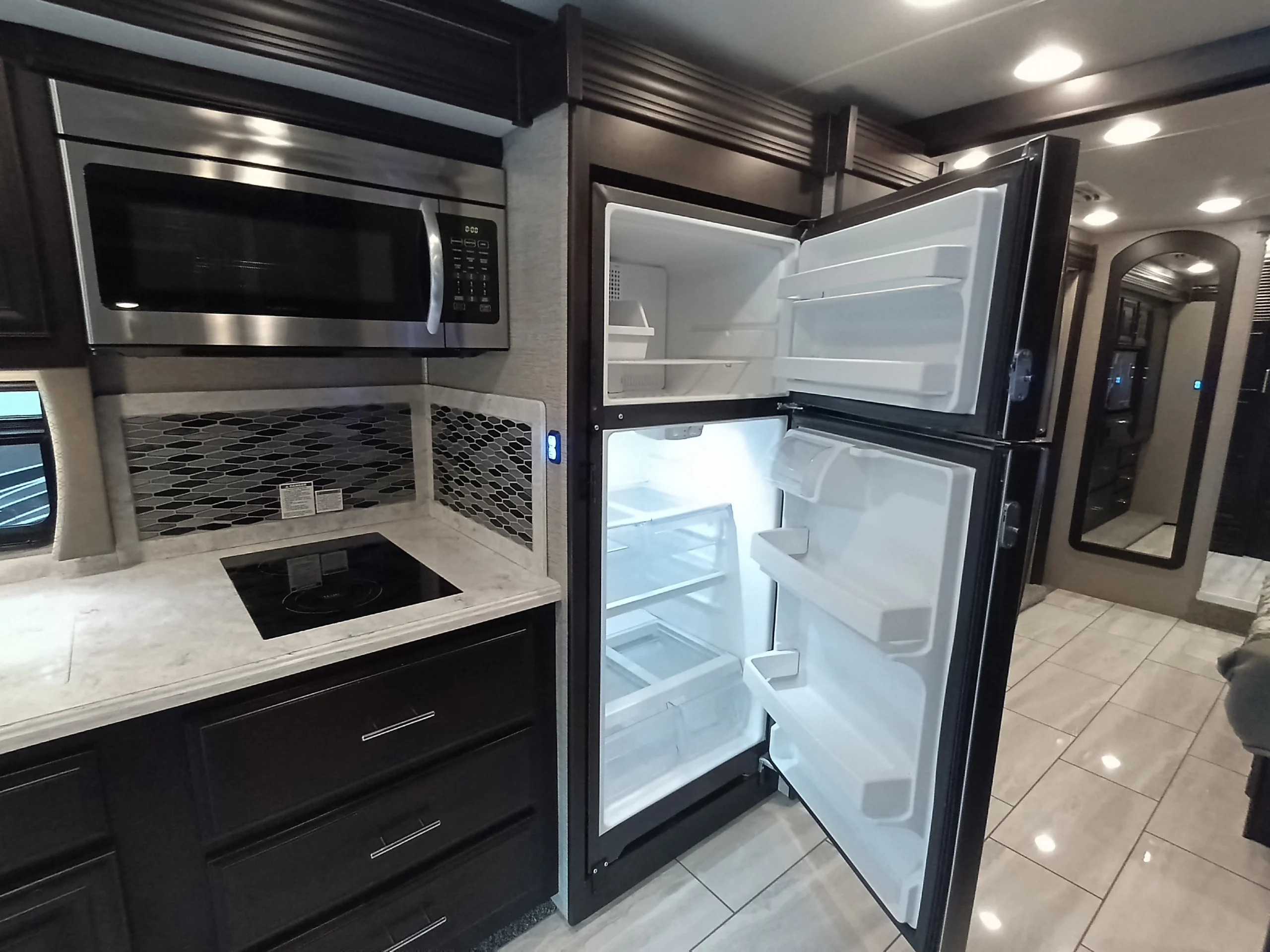 IMG_20260611_191321_209 Modern Motorcoach and RV kitchen with stainless steel microwave, open fridge, dark cabinets, and tile flooring.