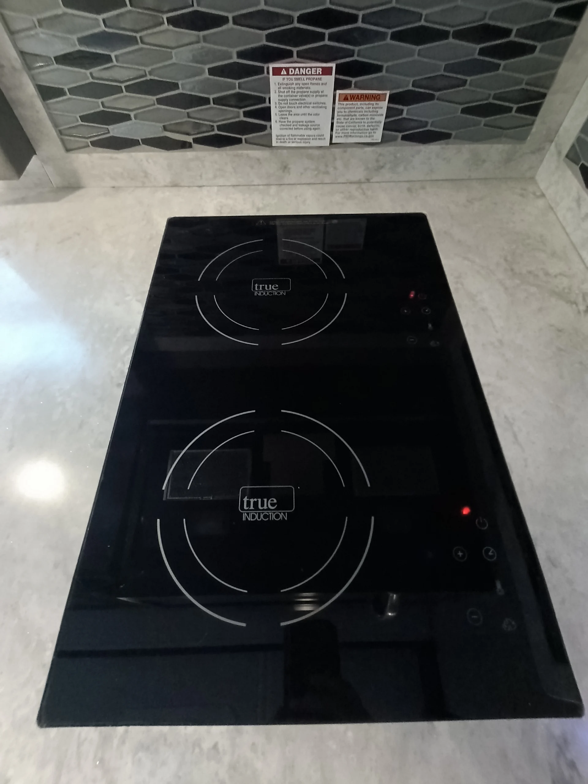 IMG_20260611_191336_460 Induction cooktop with control panel on a countertop, tiled backsplash, and safety warnings, suitable for Motorcoach and RVs.