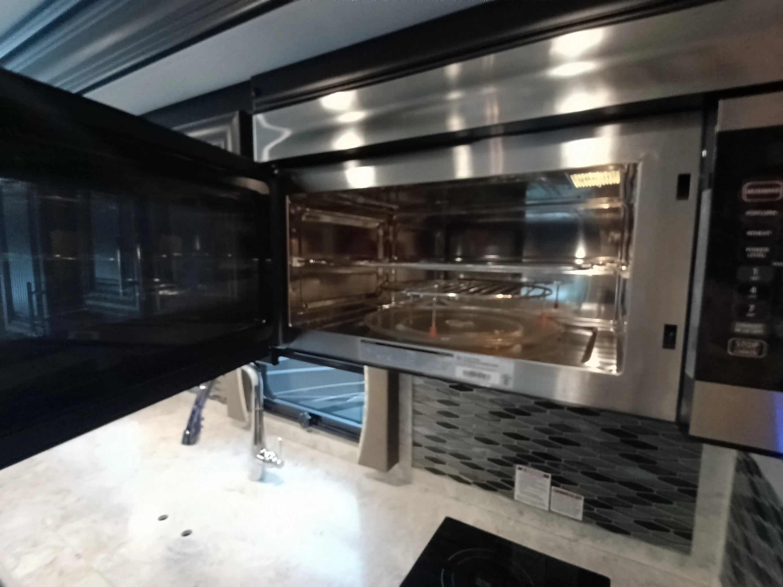 IMG_20260611_191347_717 Open stainless steel microwave in a Motorcoach and Rvs kitchen, with a sleek countertop and modern backsplash.