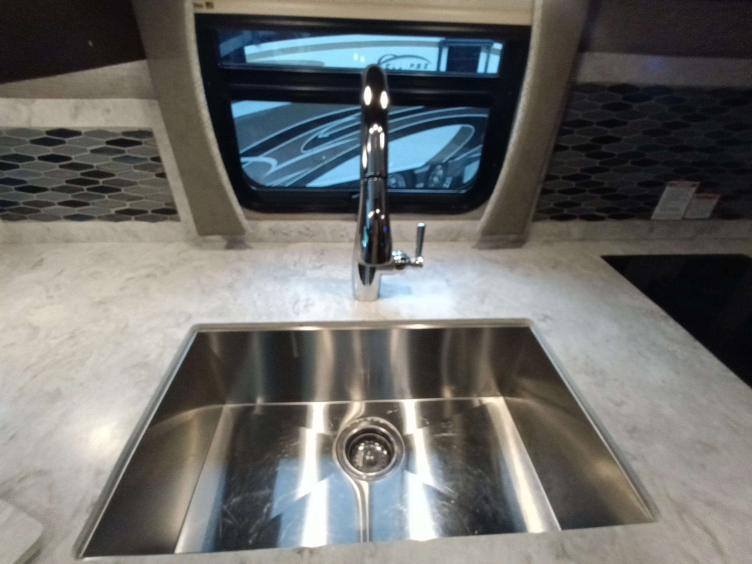 IMG_20260611_191422_237 Stainless steel sink with modern faucet on marble countertop in Motorcoach and RVs setting, with window view.