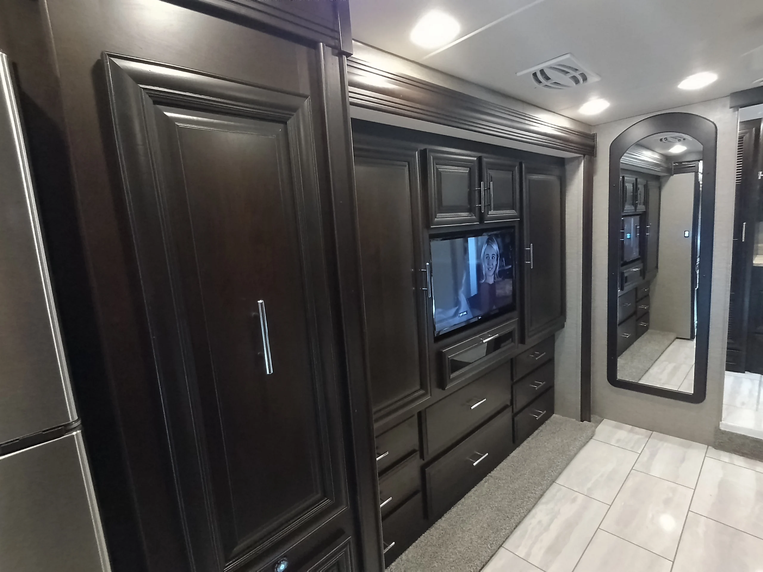 IMG_20260611_191449_083 Luxurious Motorcoach interior with dark wood cabinets, built-in TV, large mirror, and tiled floor.