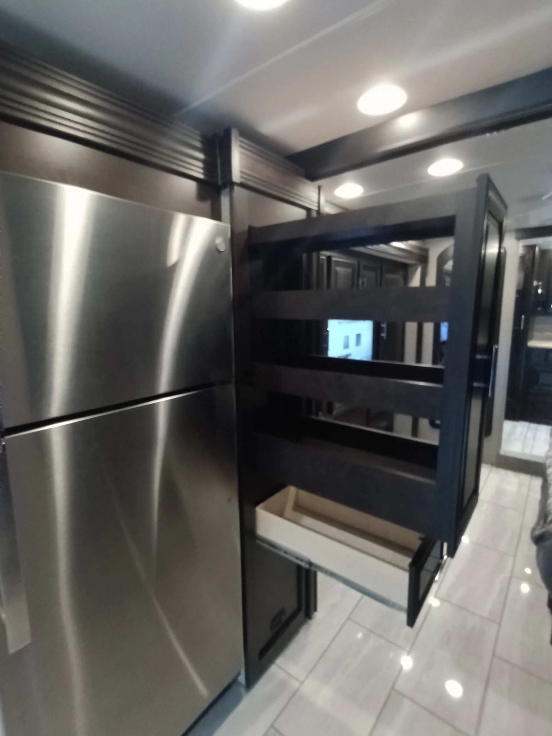 IMG_20260611_191511_063 Sleek RV kitchen with stainless steel fridge, open pull-out pantry drawer, and modern lighting, enhancing motorcoach convenience.