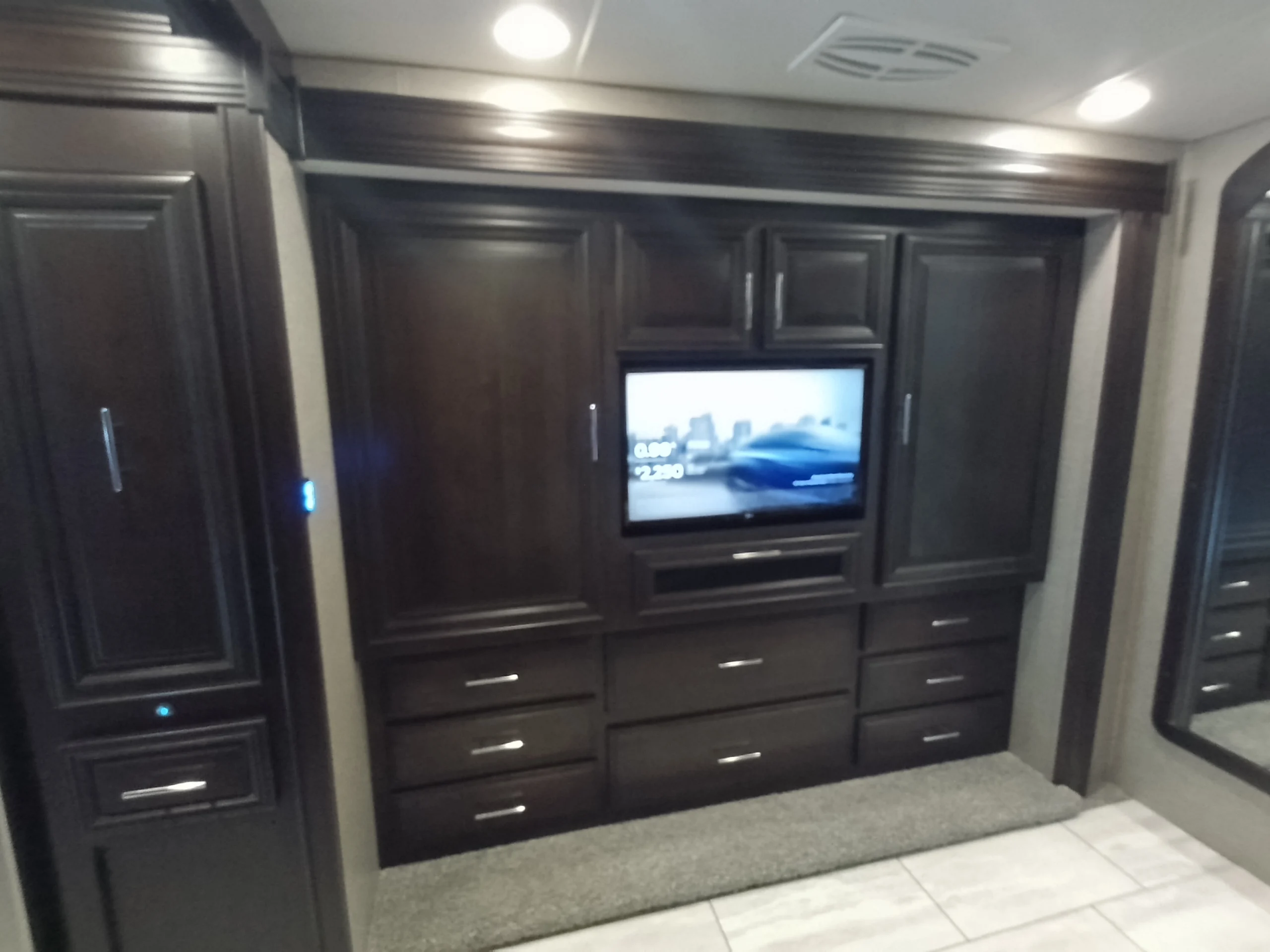 IMG_20260611_191734_923 Luxurious Motorcoach interior with dark wood cabinets, integrated TV, and modern lighting, showcasing RV elegance.