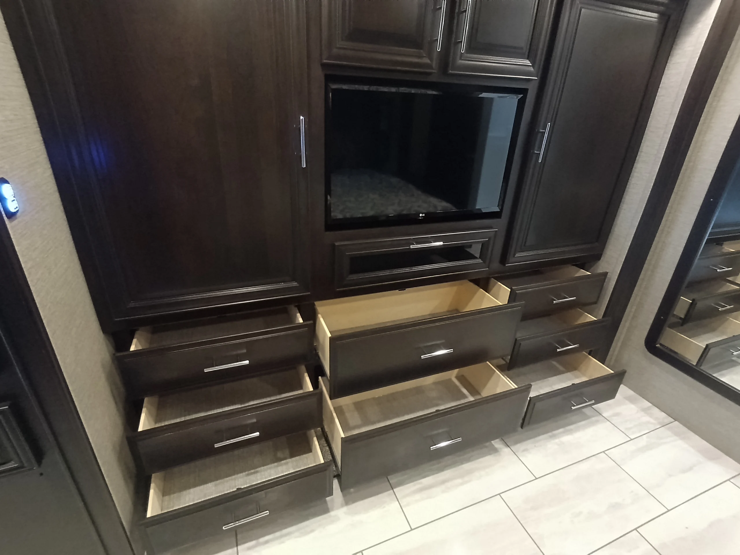 IMG_20260611_191844_544 Dark wood cabinetry and open drawers in a Motorcoach and RVs interior, with a TV centered above drawers on tiled flooring.