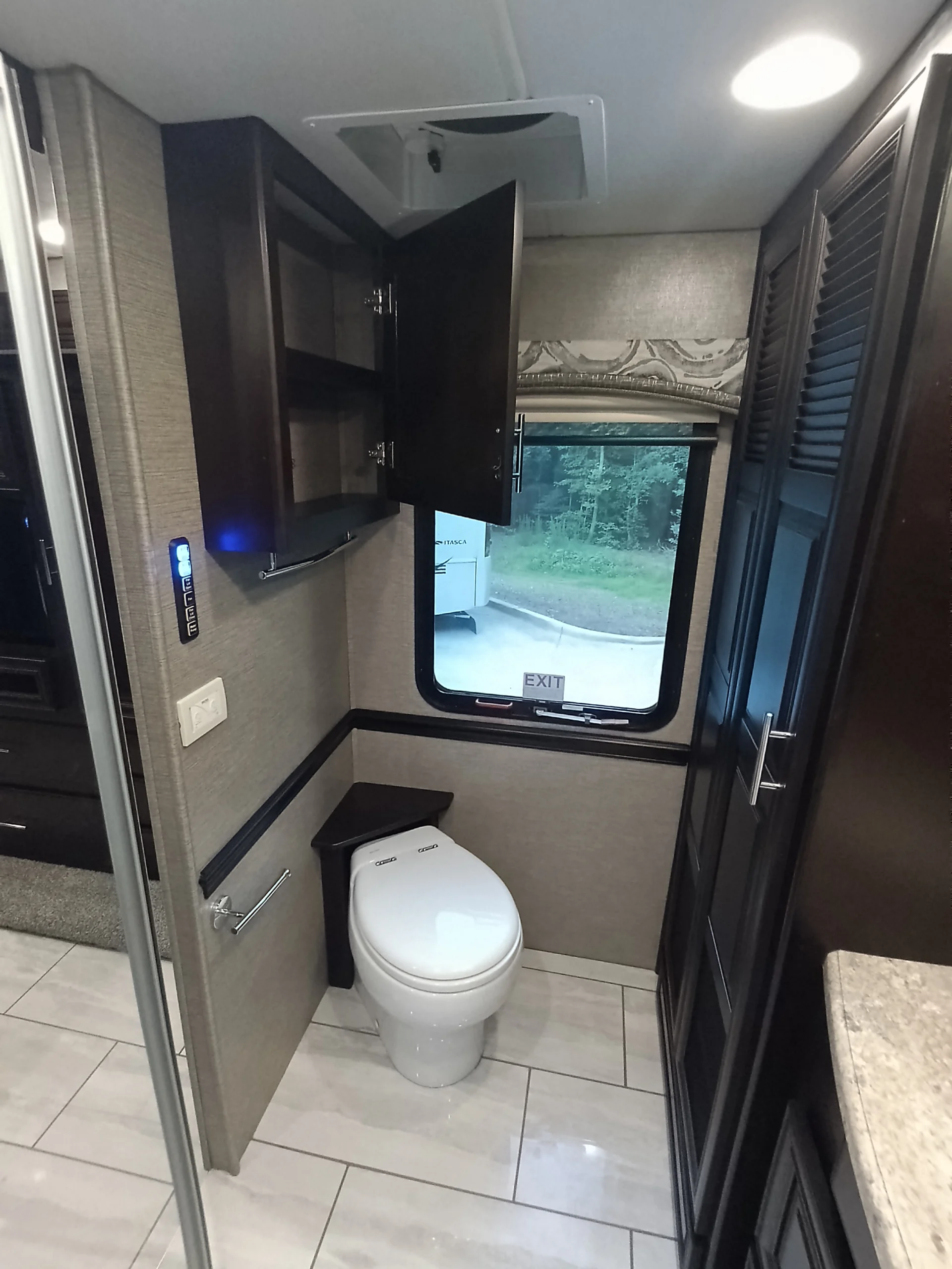IMG_20260611_192001_185 Modern RV bathroom with a toilet, open dark wood cabinet, window, and tiled floor. Motorcoach and RVs interior features sleek design.