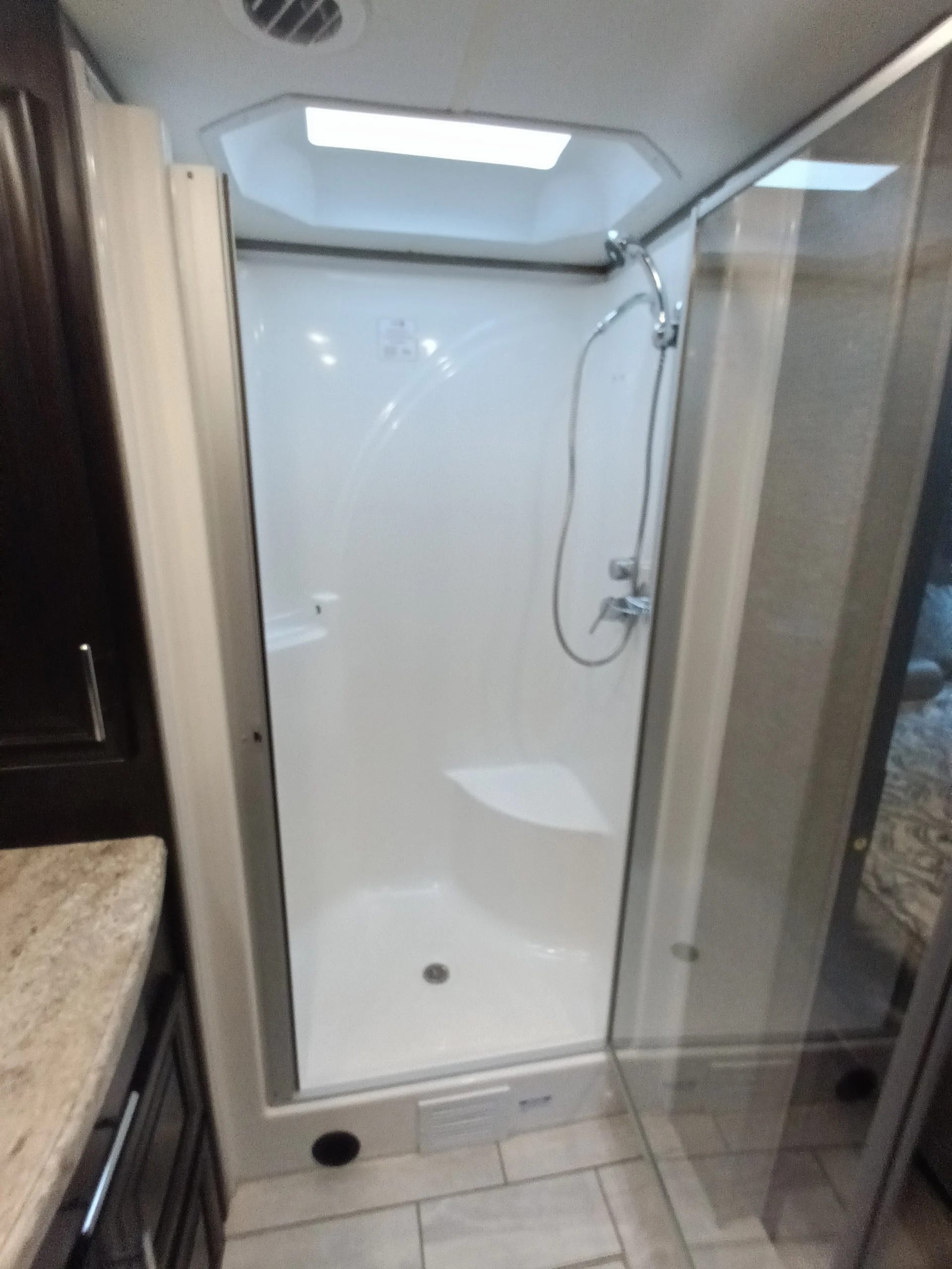 IMG_20260611_192012_708 Spacious RV shower with glass doors, skylight, and chrome fixtures, part of a Motorcoach and Rvs setup, alongside a granite countertop.