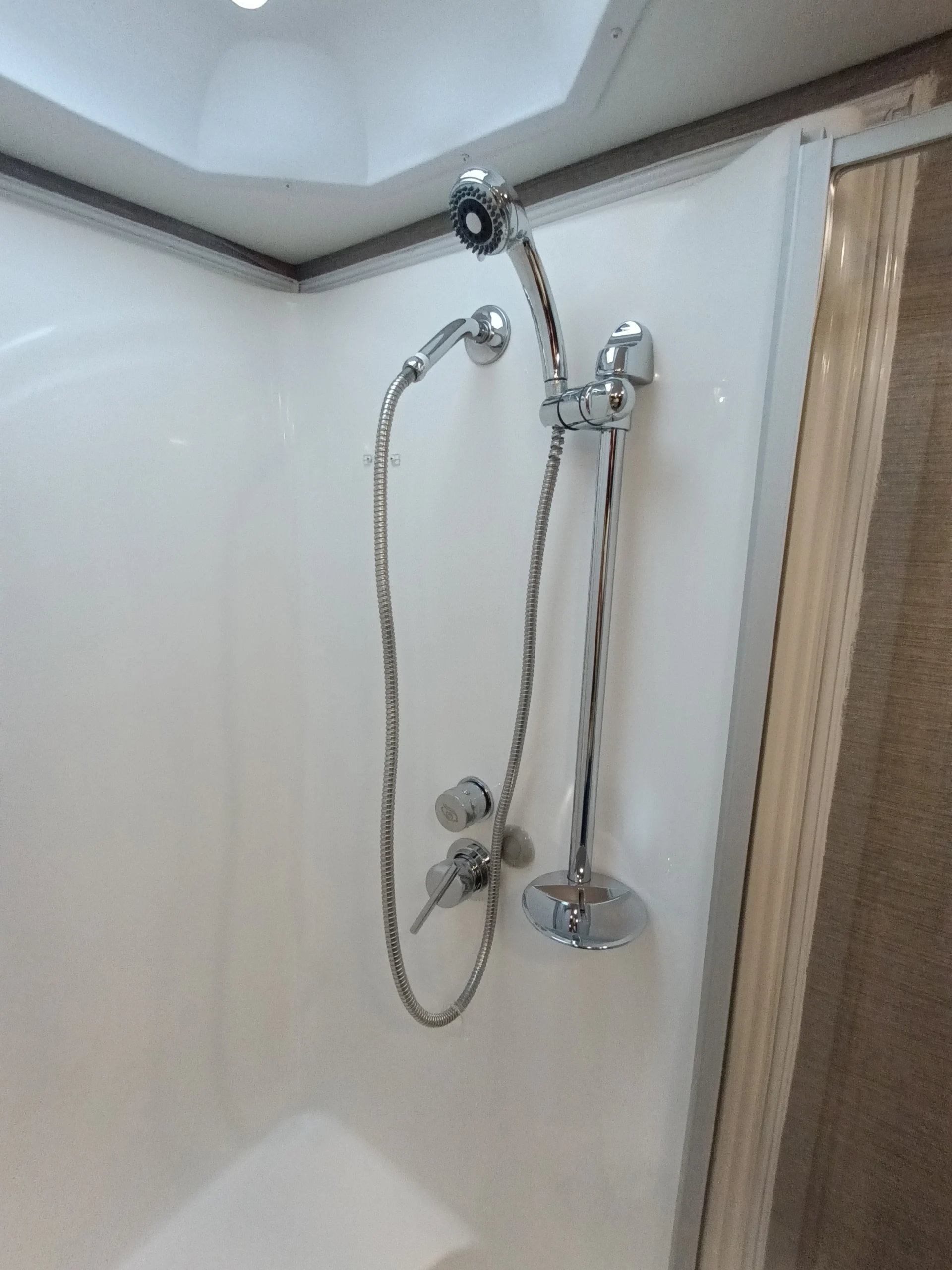 IMG_20260611_192019_498 Compact shower with adjustable showerhead and hose, typical for Motorcoach and RVs, featuring chrome fixtures and a white interior.