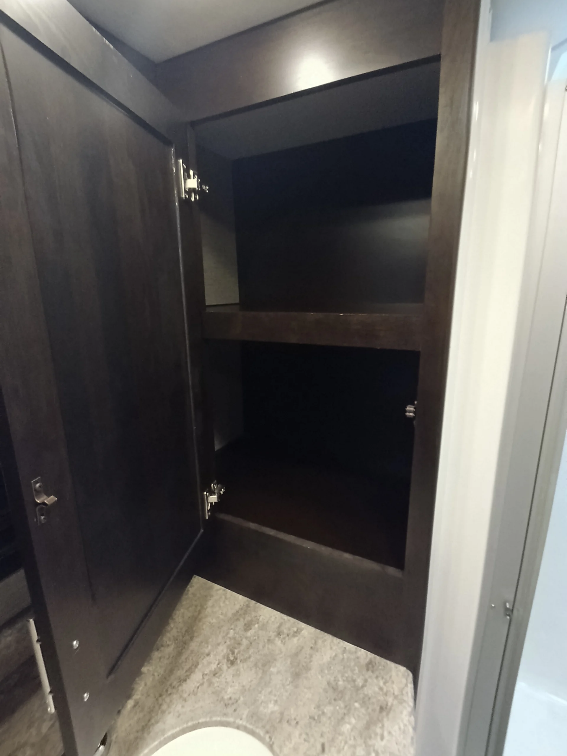 IMG_20260611_192030_337 Open dark wood cabinet with shelves inside a Motorcoach and RVs bathroom, next to a countertop.