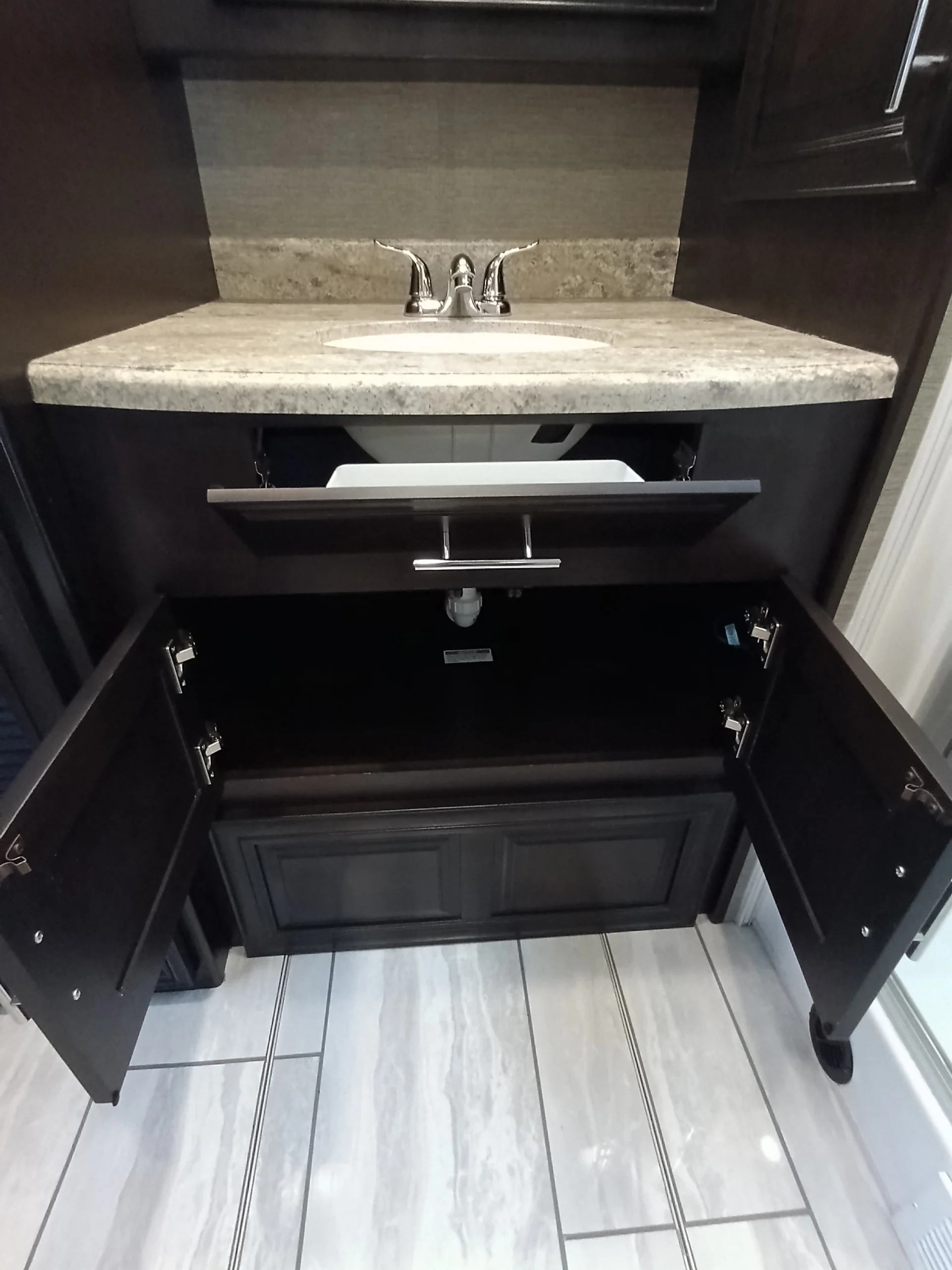 IMG_20260611_192058_842 RV bathroom sink with open cabinet doors and drawer, revealing storage under a marble countertop. Ideal for Motorcoach and RVs.