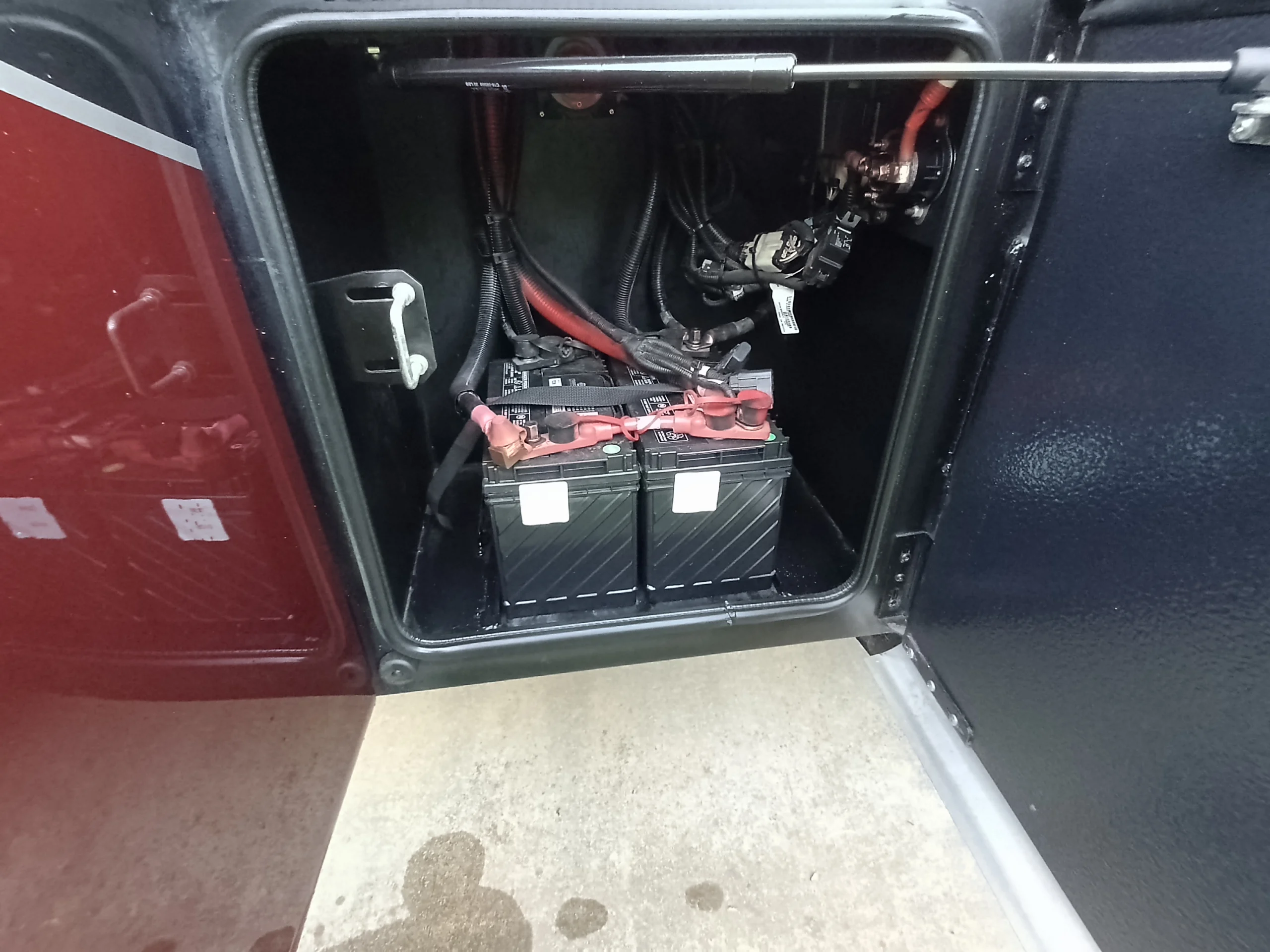 IMG_20260611_194114_794 Open compartment of a motorcoach revealing dual batteries and wiring, highlighting essential RV power components.