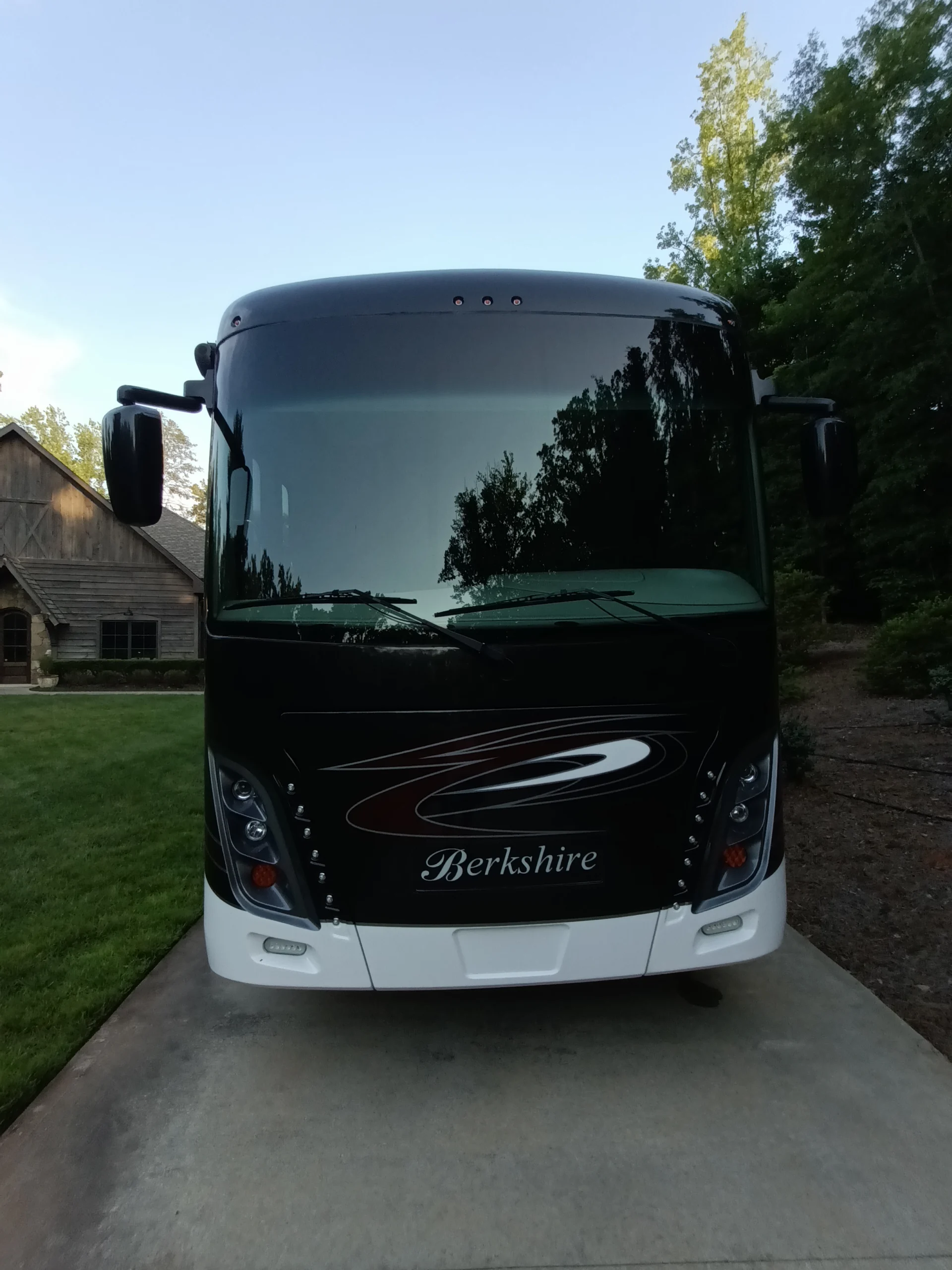 IMG_20260611_194253_619 Front view of a black Berkshire motorcoach, parked on a paved driveway, with trees and a building in the background.