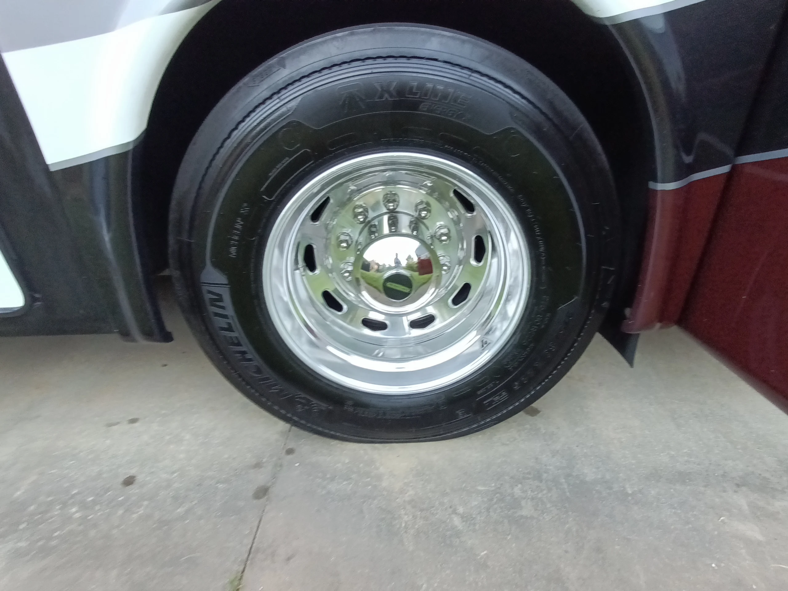 IMG_20260611_194716_567 Shiny chrome wheel with Michelin tire on a Motorcoach and RVs, parked on concrete.