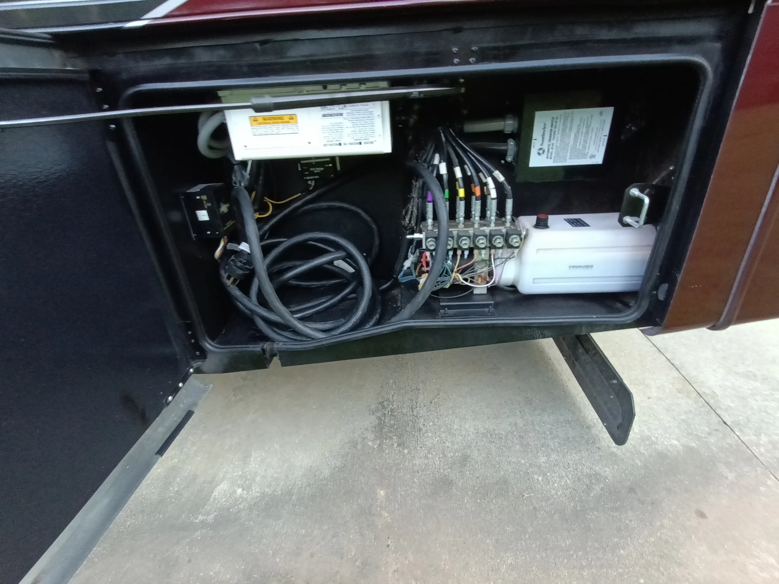IMG_20260611_194728_286 Open compartment on a motorcoach shows cables, wiring, and a fluid reservoir, highlighting the complex systems in Motorcoach and RVs.