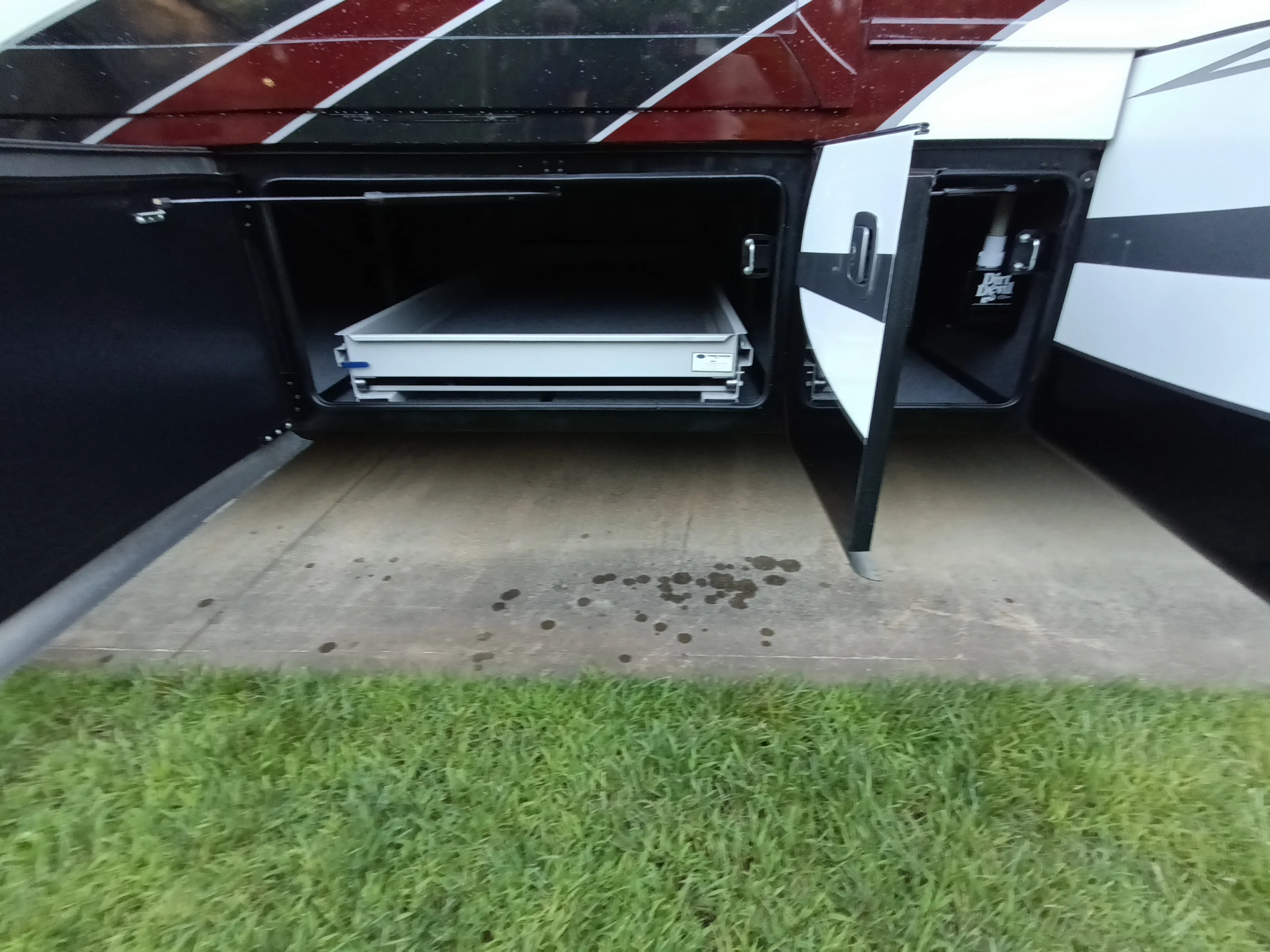 IMG_20260611_194736_944 Open storage compartments in a Motorcoach and Rvs vehicle, with pull-out drawers and grass in foreground.