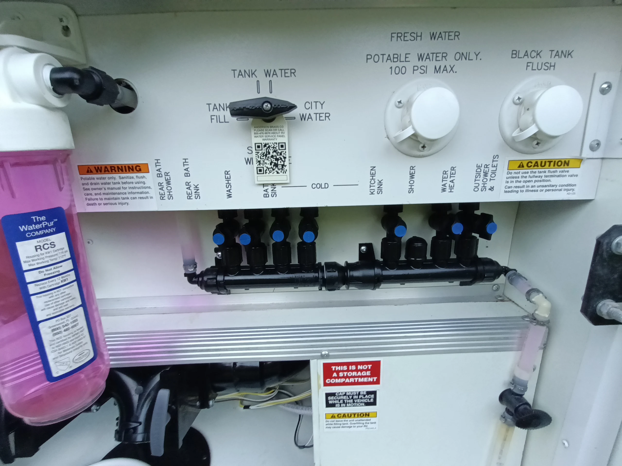 IMG_20260611_194837_253 RV water control panel with tank fill and flush knobs, labeled for kitchen, shower, and bath, alongside a water purification filter.