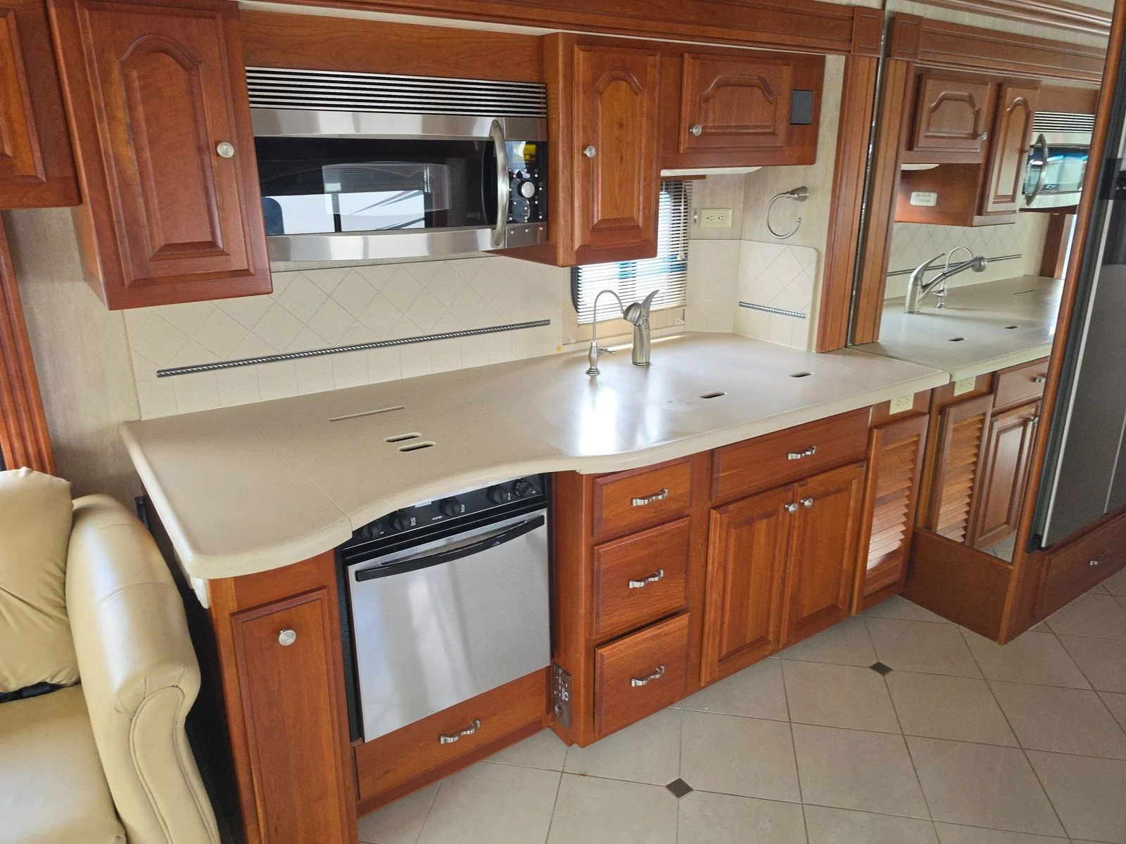 20260831171446-206ae319-b0d0-4323-aaa0-097aca835768 Spacious RV kitchen with wooden cabinets, countertop, microwave, and stove, reflecting in a mirrored wall. Ideal for Motorcoach and RVs.