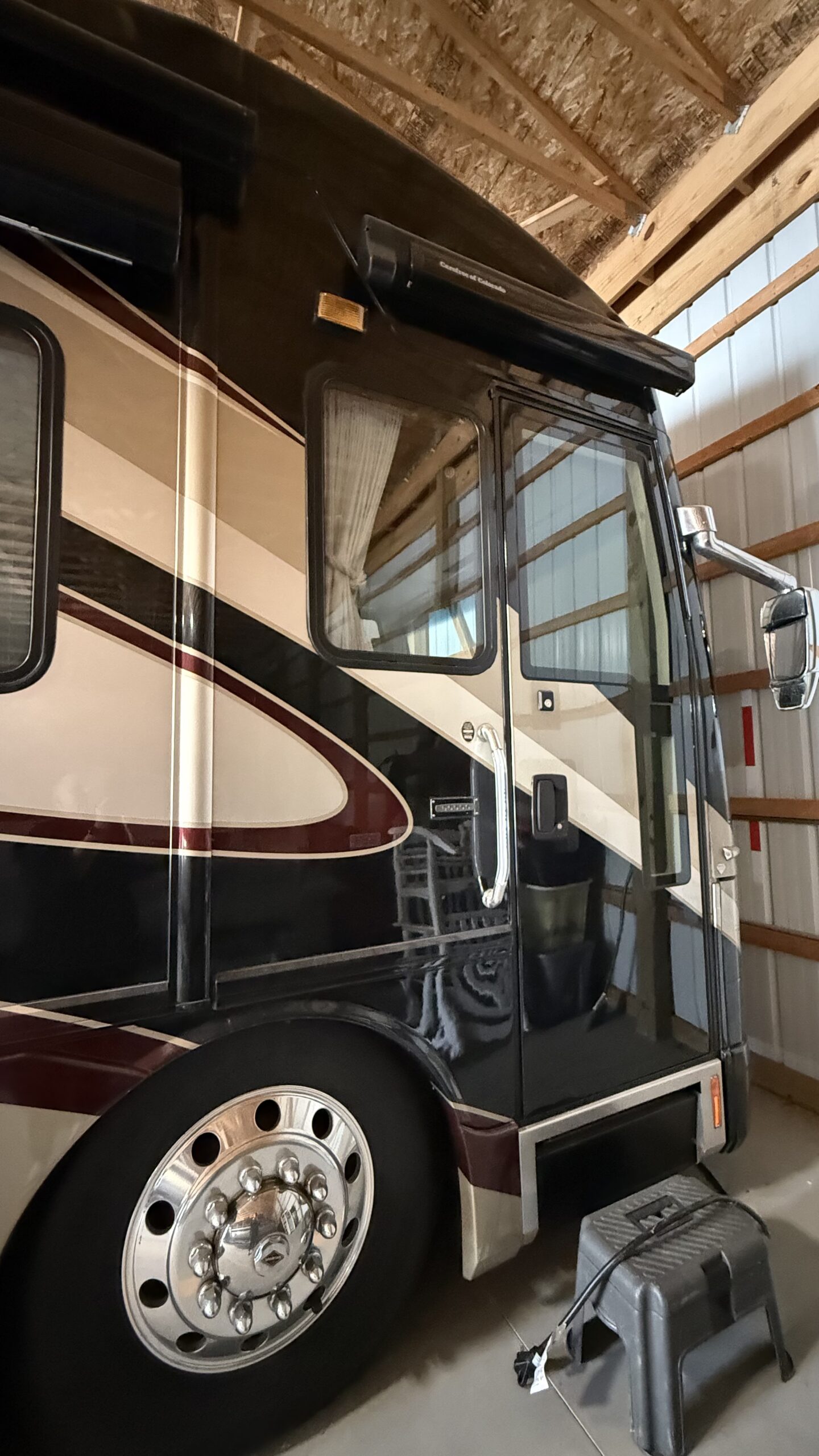 Motorcoach parked in a garage with a step stool and cord nearby, showcasing detailed design and large side mirror.