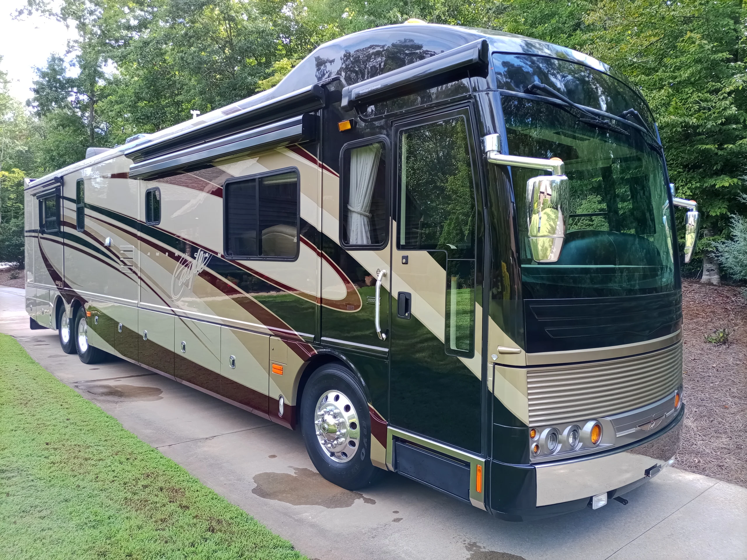 IMG_20260922_153707_191 Luxurious motorcoach with sleek design, parked on a driveway surrounded by lush greenery.