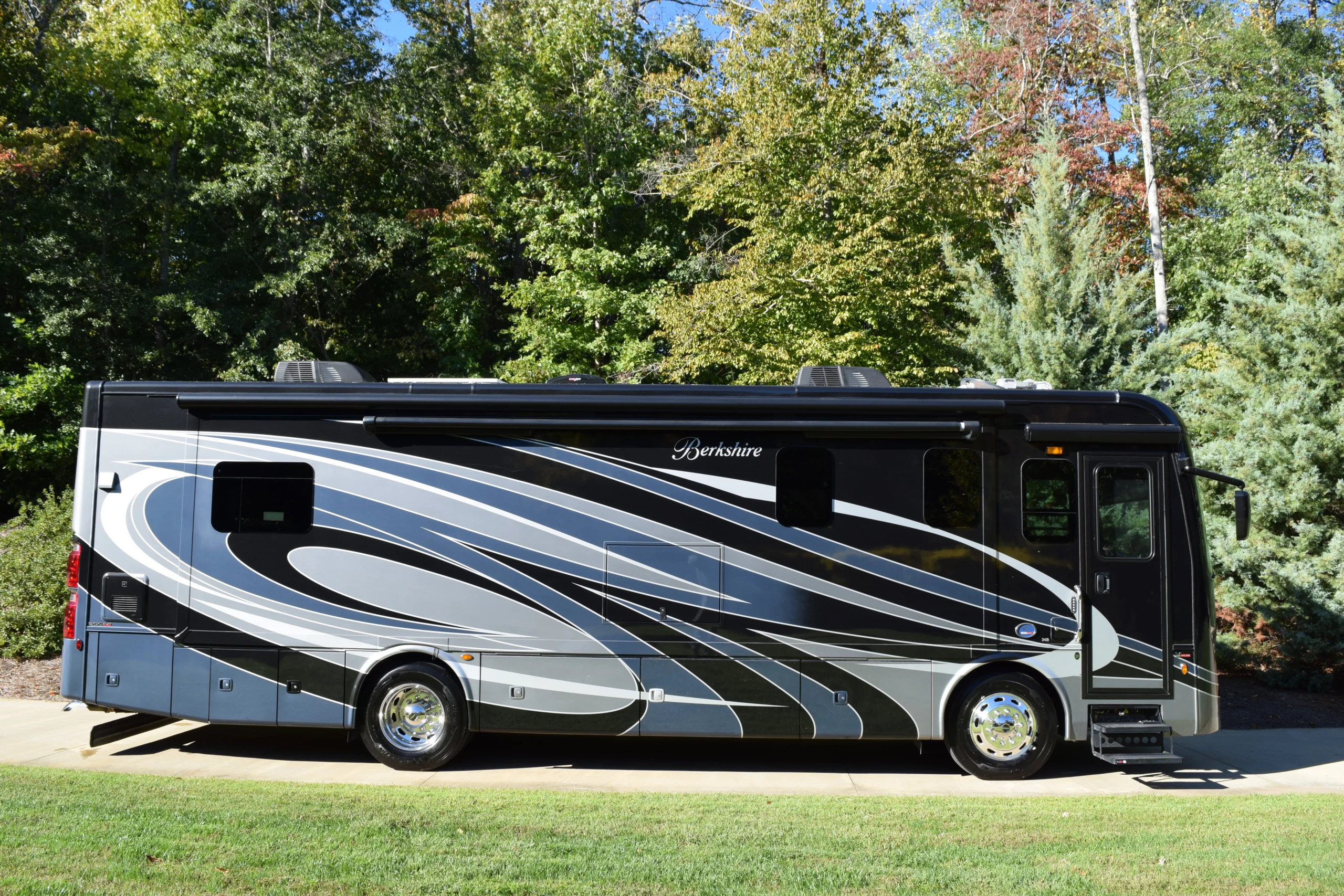 DSC_0690 Luxury motorcoach with sleek black and silver design parked on driveway, surrounded by lush green trees.