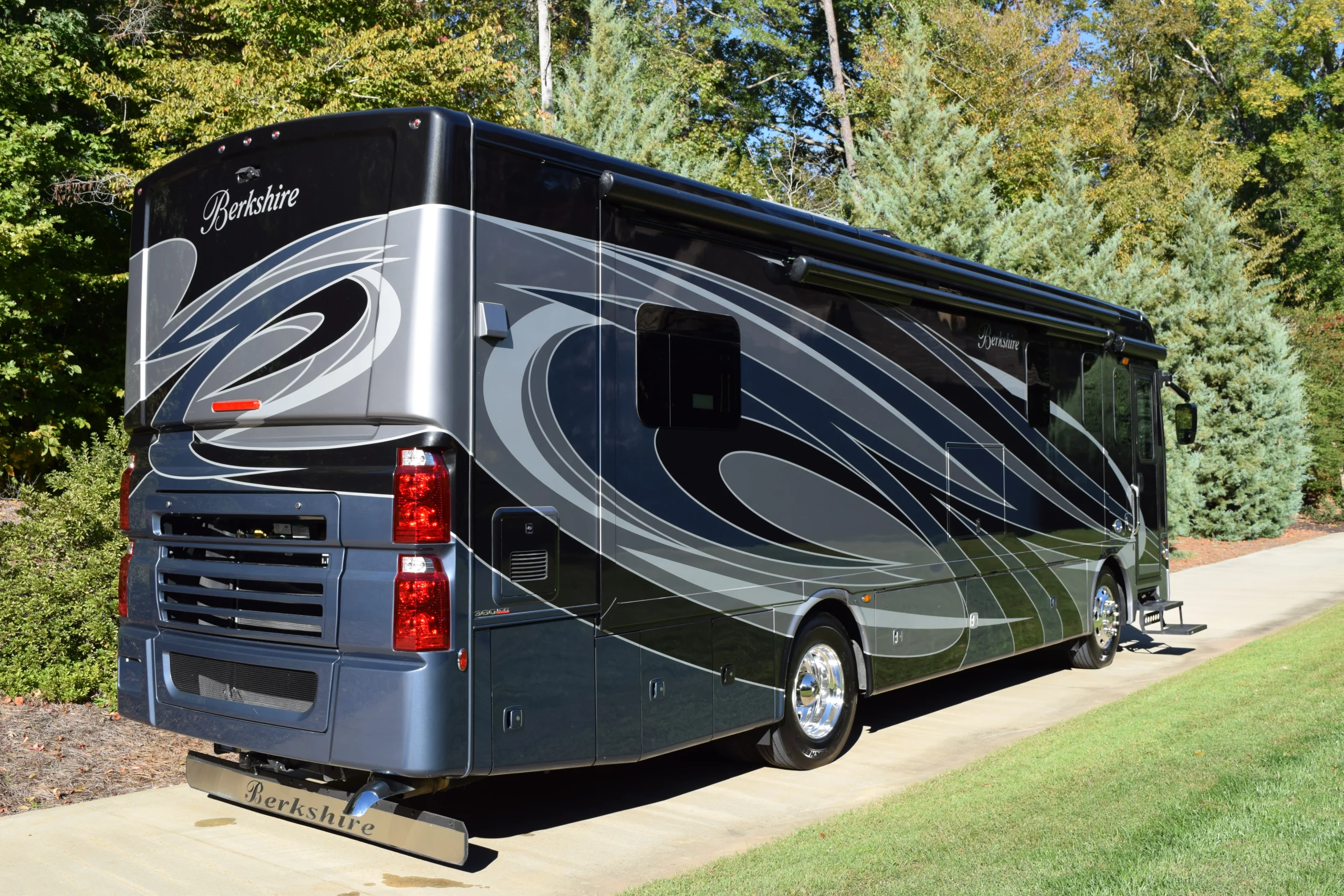 DSC_0692 Luxury Berkshire motorcoach parked on driveway, featuring sleek design and swirling graphics, surrounded by lush greenery.