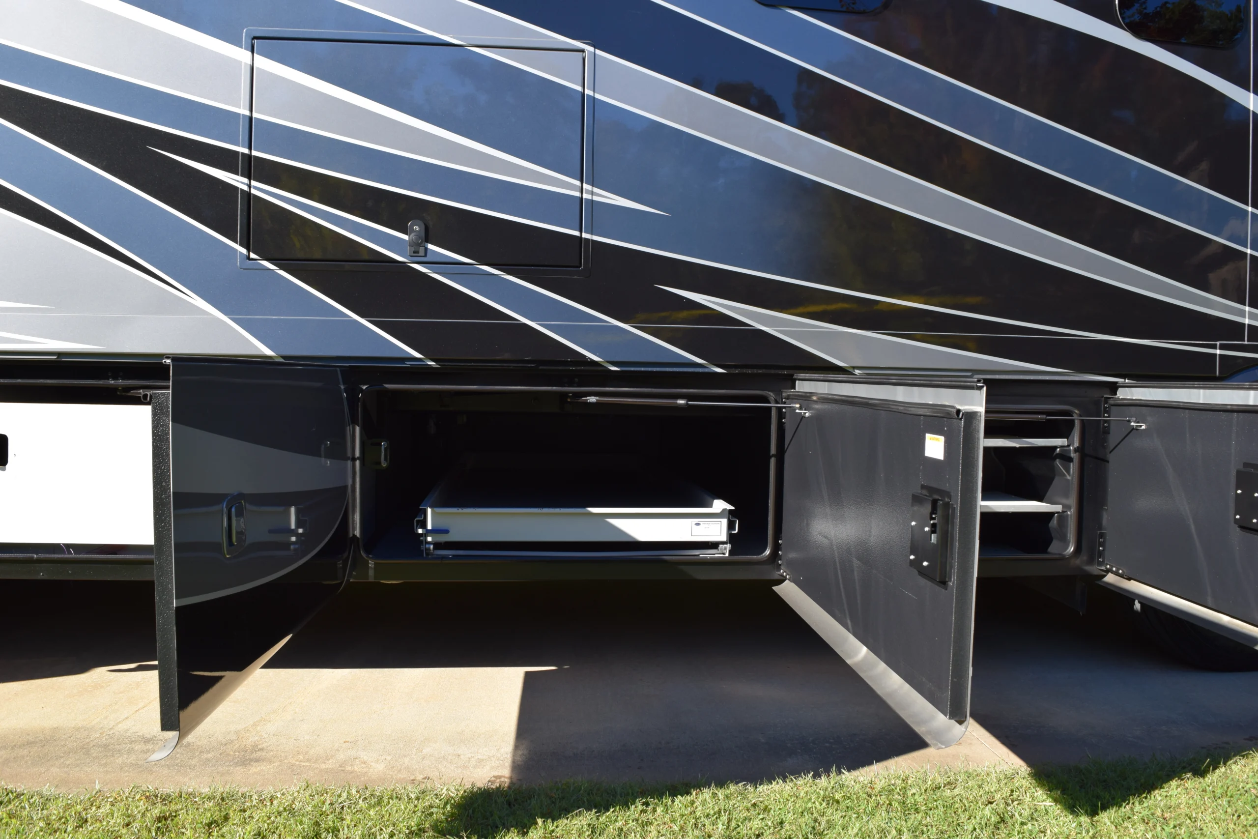 DSC_0696 Open storage compartments beneath a Motorcoach and RV, showcasing spacious slide-out trays, with a sleek black and silver exterior design.