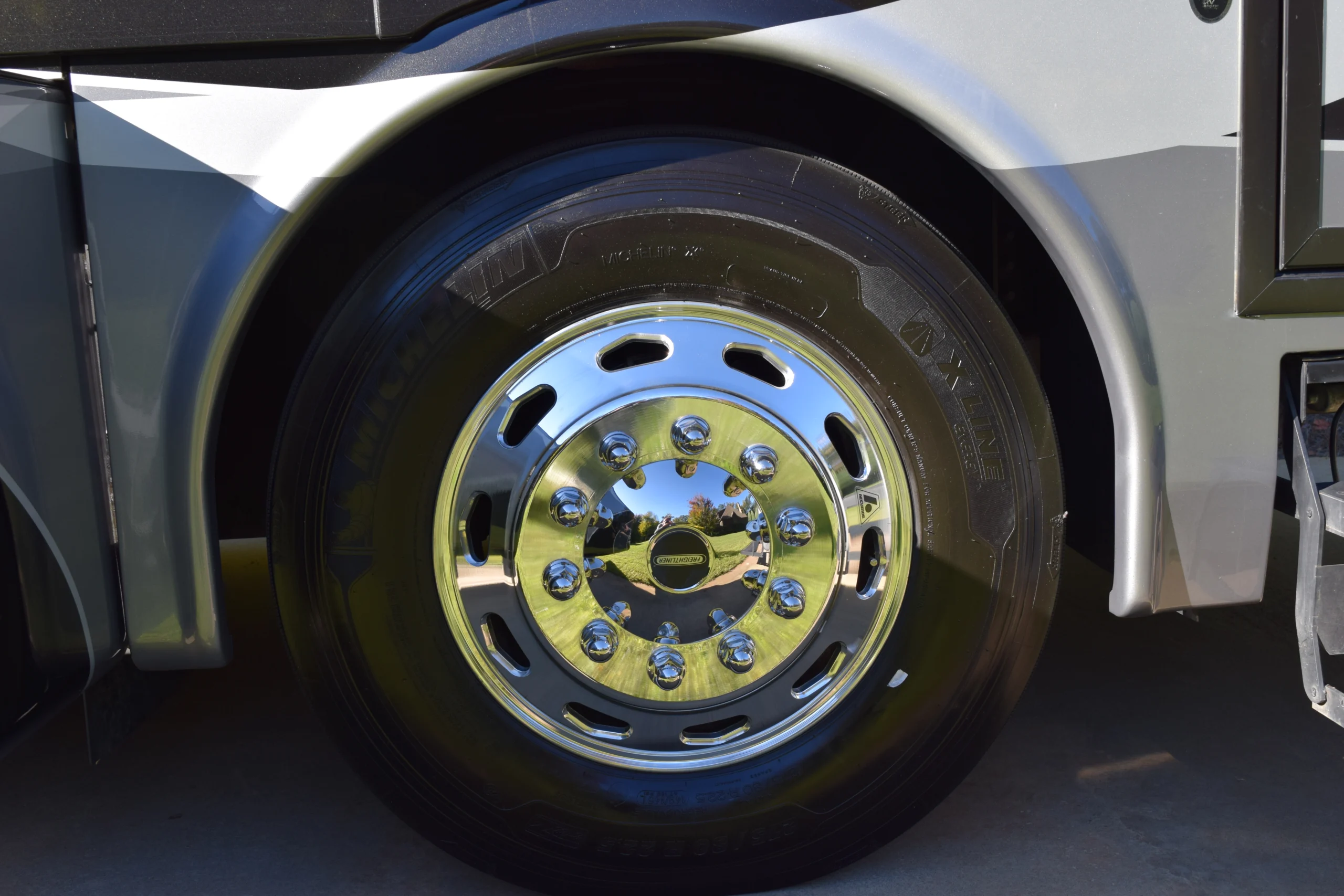 DSC_0699 Shiny chrome wheel on a Motorcoach and Rvs vehicle, reflecting greenery and sky, with a visible tire tread.