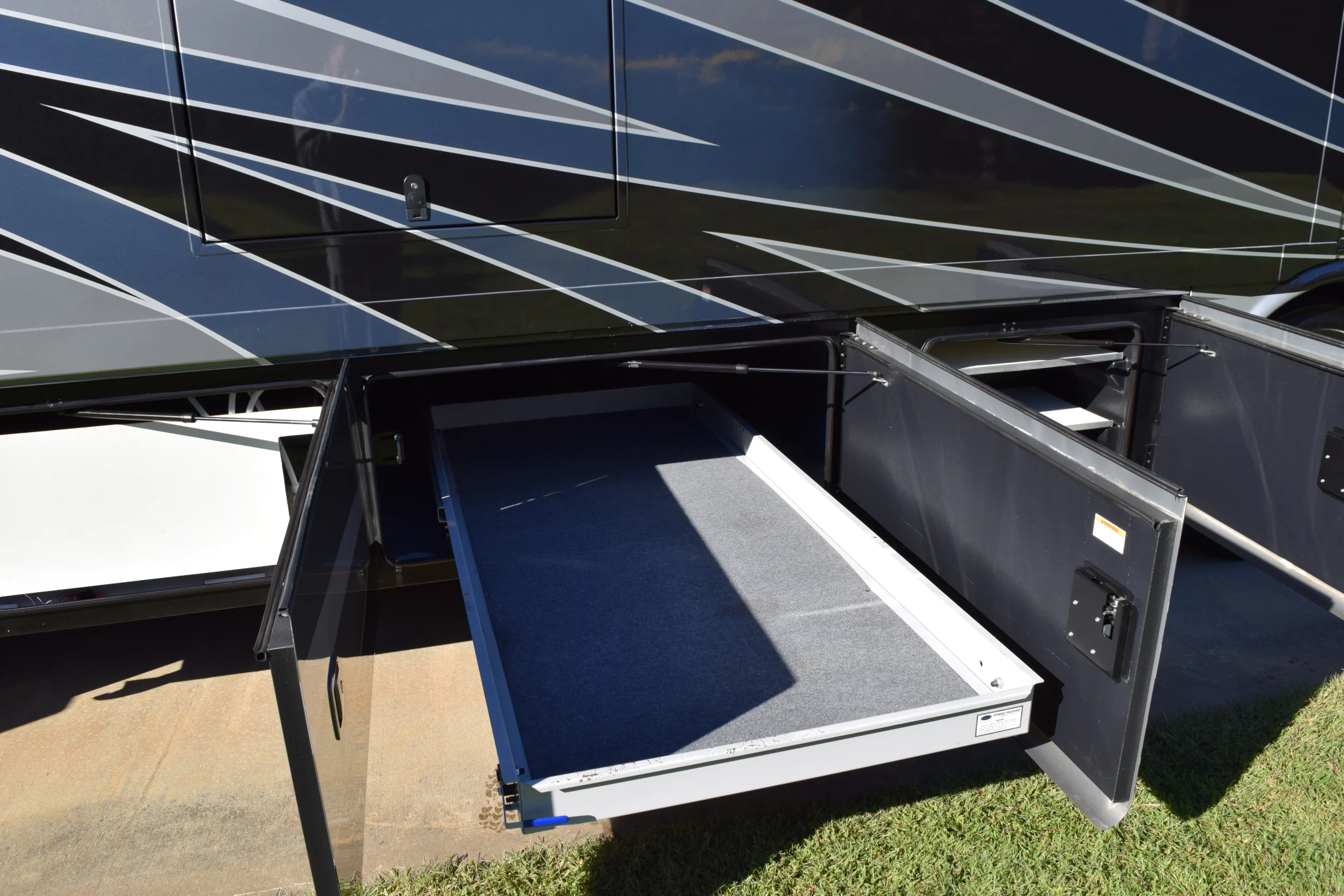 DSC_0700 Open storage compartment in a motorcoach with a sliding tray, featuring sleek, dark exterior with white and gray diagonal stripes.
