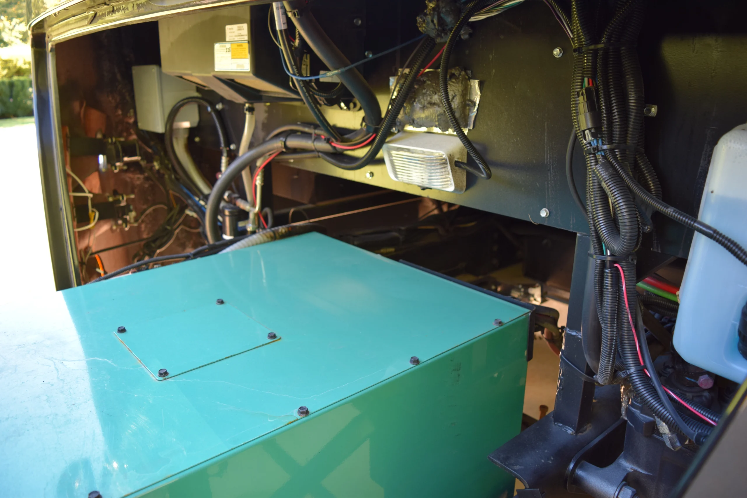 DSC_0707 Close-up of an RV or motorcoach generator compartment, showcasing wiring, tubes, and a prominent teal component.