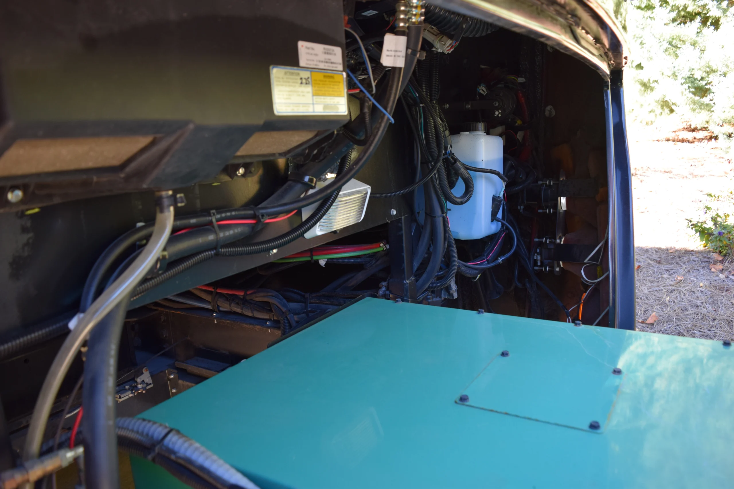 DSC_0708 Inside motorcoach compartment with various wires and components visible, including a green power unit and a white fluid reservoir.