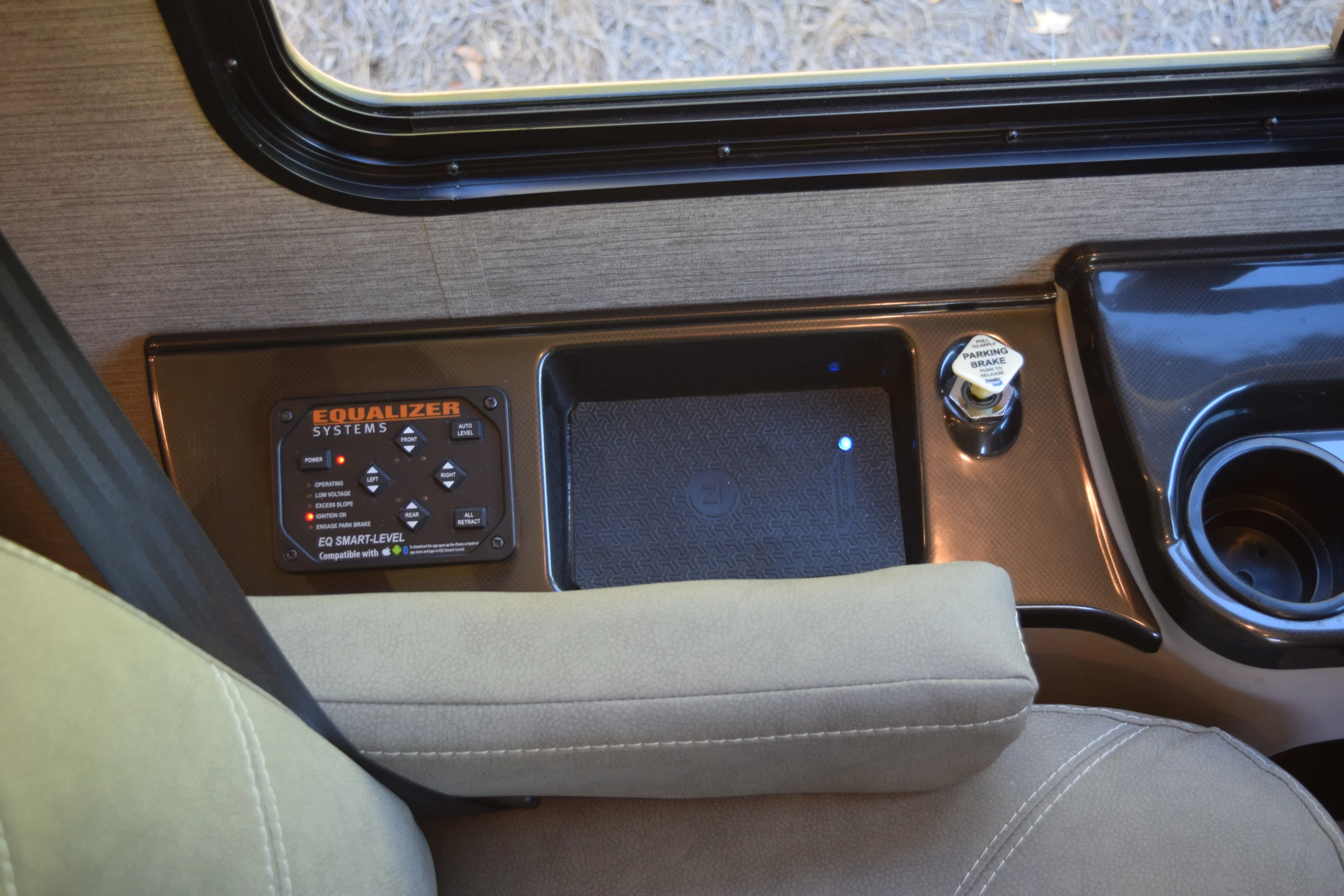 DSC_0716 Motorcoach control panel with Equalizer Systems buttons, parking brake knob, and cup holder near a window.