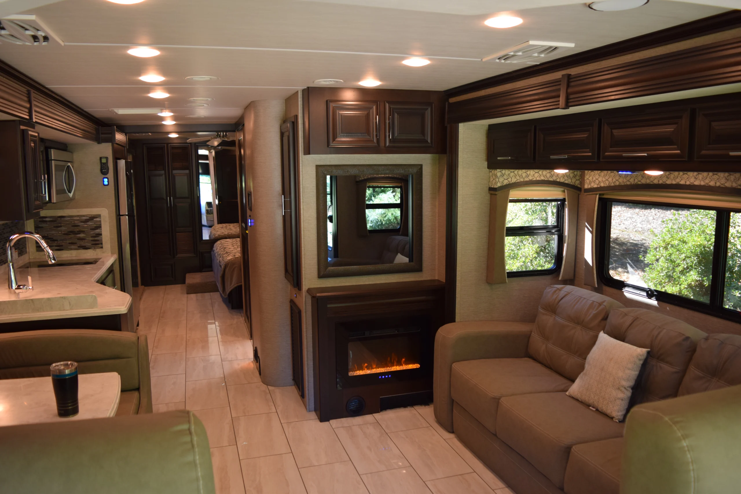 DSC_0728 Luxurious Motorcoach interior, featuring a modern kitchen, cozy sofa, electric fireplace, and ample windows with outside greenery.