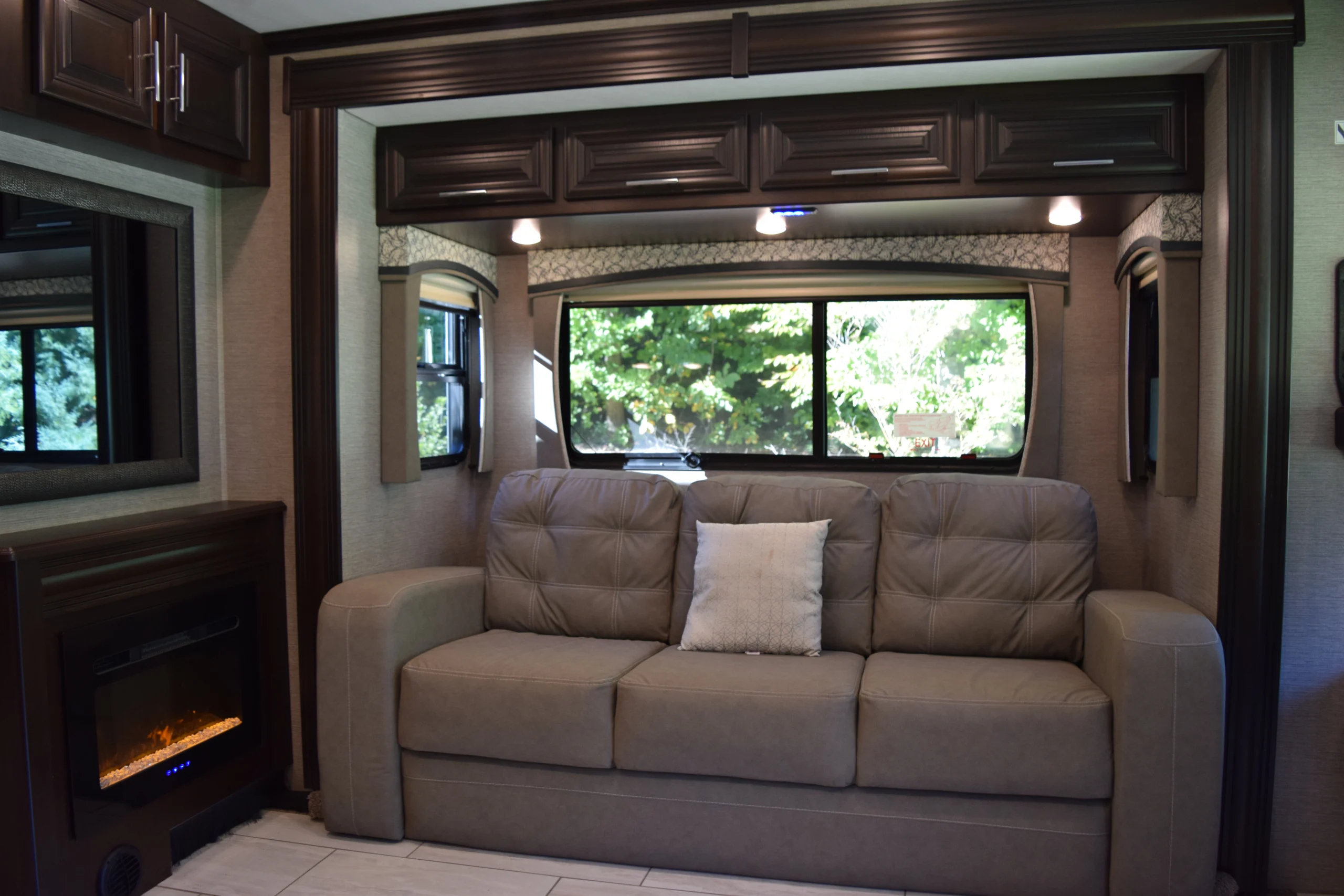 DSC_0730 Motorcoach and RV interior with a beige sofa, decorative pillow, electric fireplace, and large window with greenery outside.