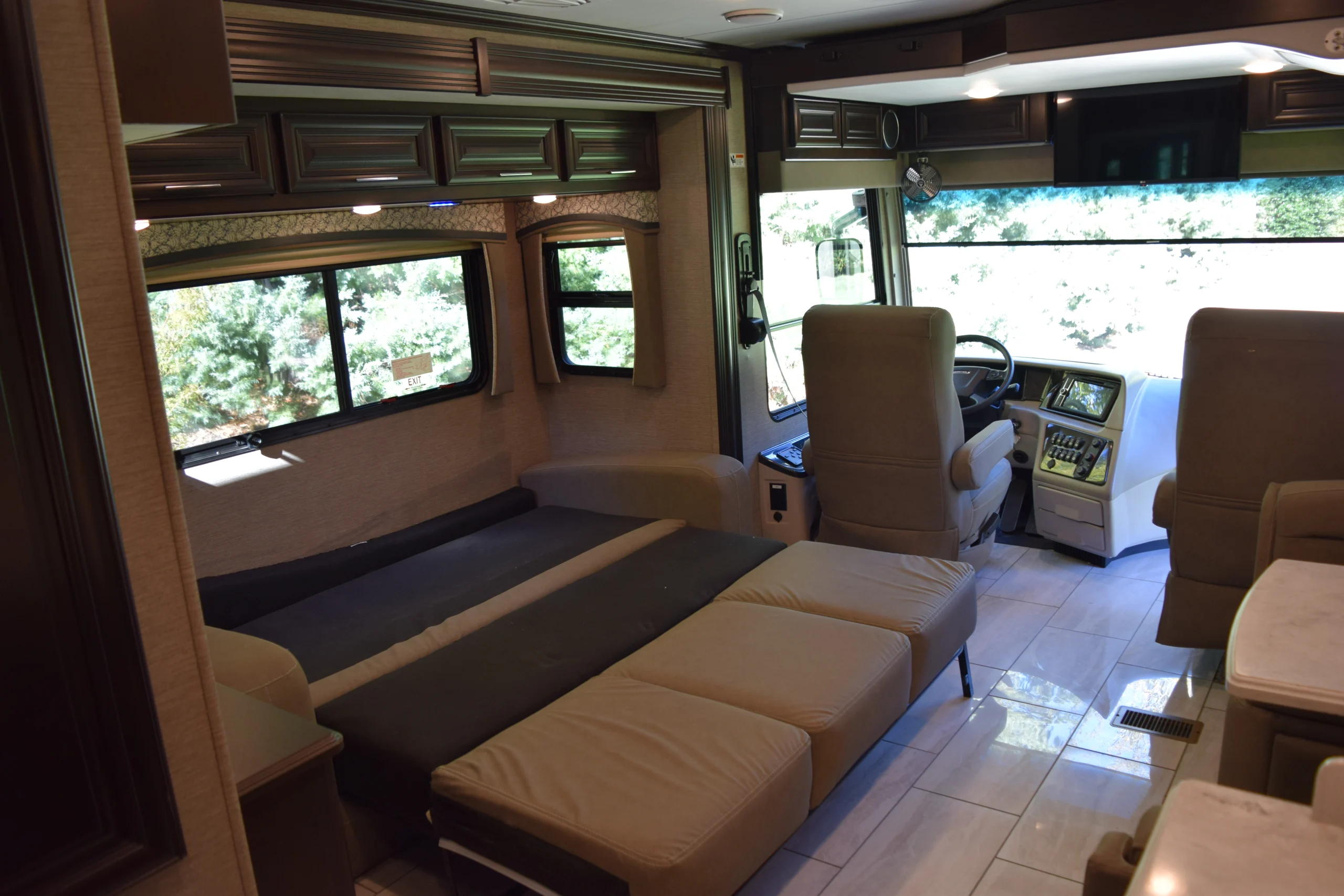DSC_0731 Luxurious Motorcoach interior with plush beige seating, convertible sofa bed, large windows, and driver's cockpit, offering comfort and style.