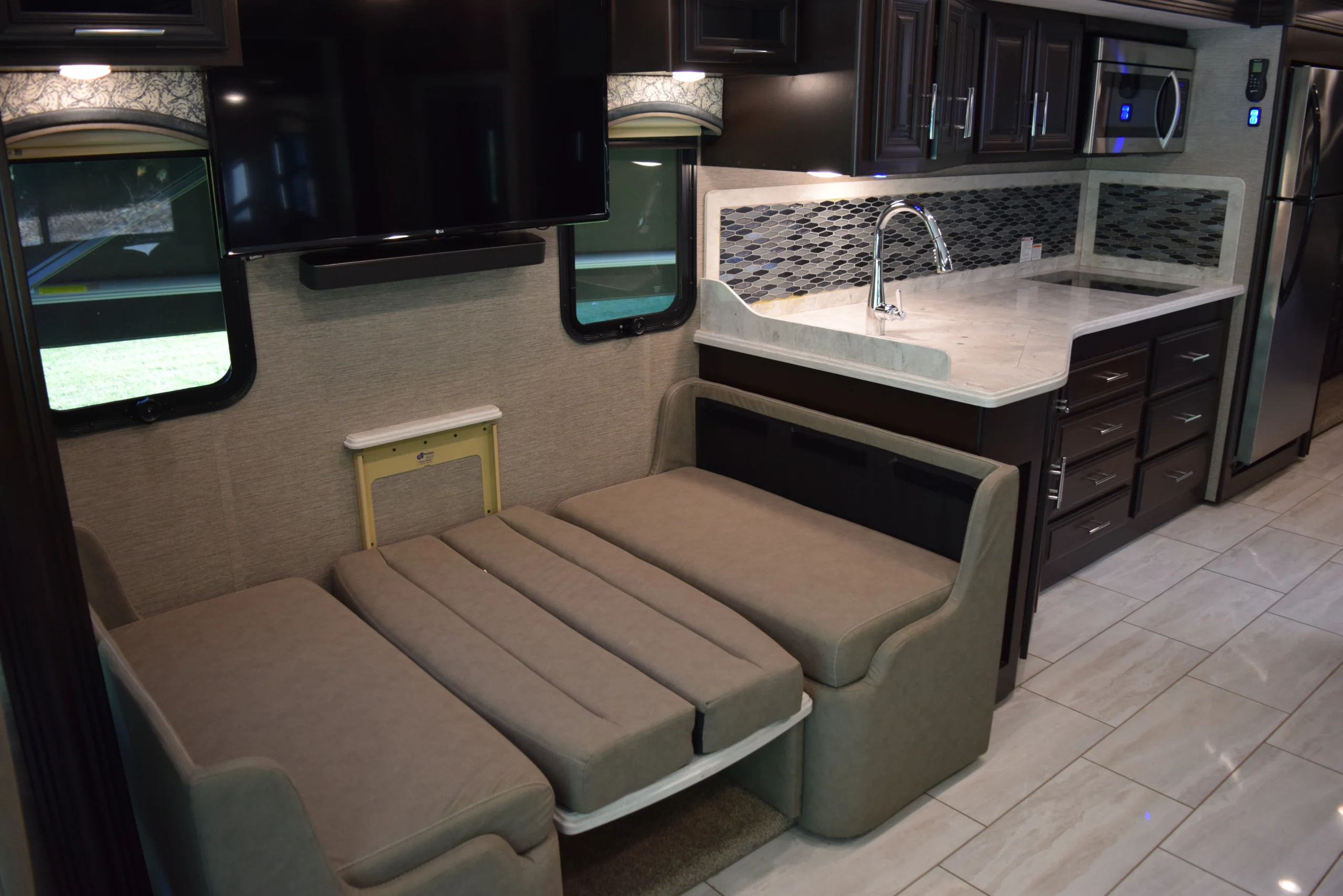 DSC_0733 RV interior with a fold-out bed, modern cabinets, large TV, and sleek kitchenette, ideal for motorcoach and RV enthusiasts.