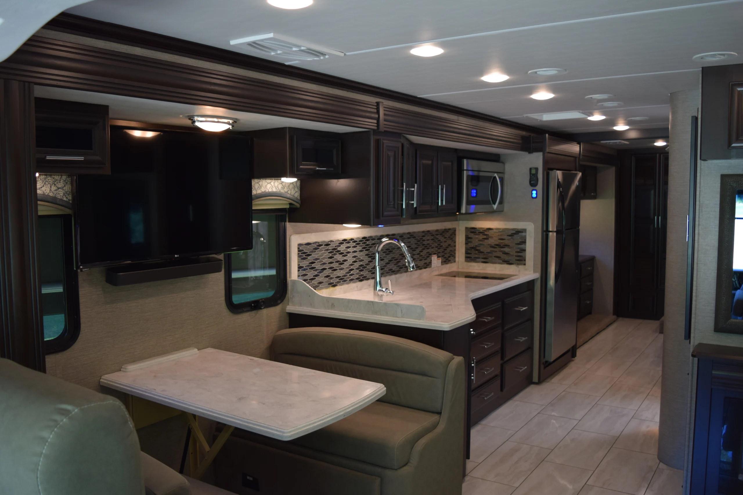 DSC_0735 Luxurious Motorcoach interior with a modern kitchen, dark cabinets, marble countertops, and a cozy dining area.