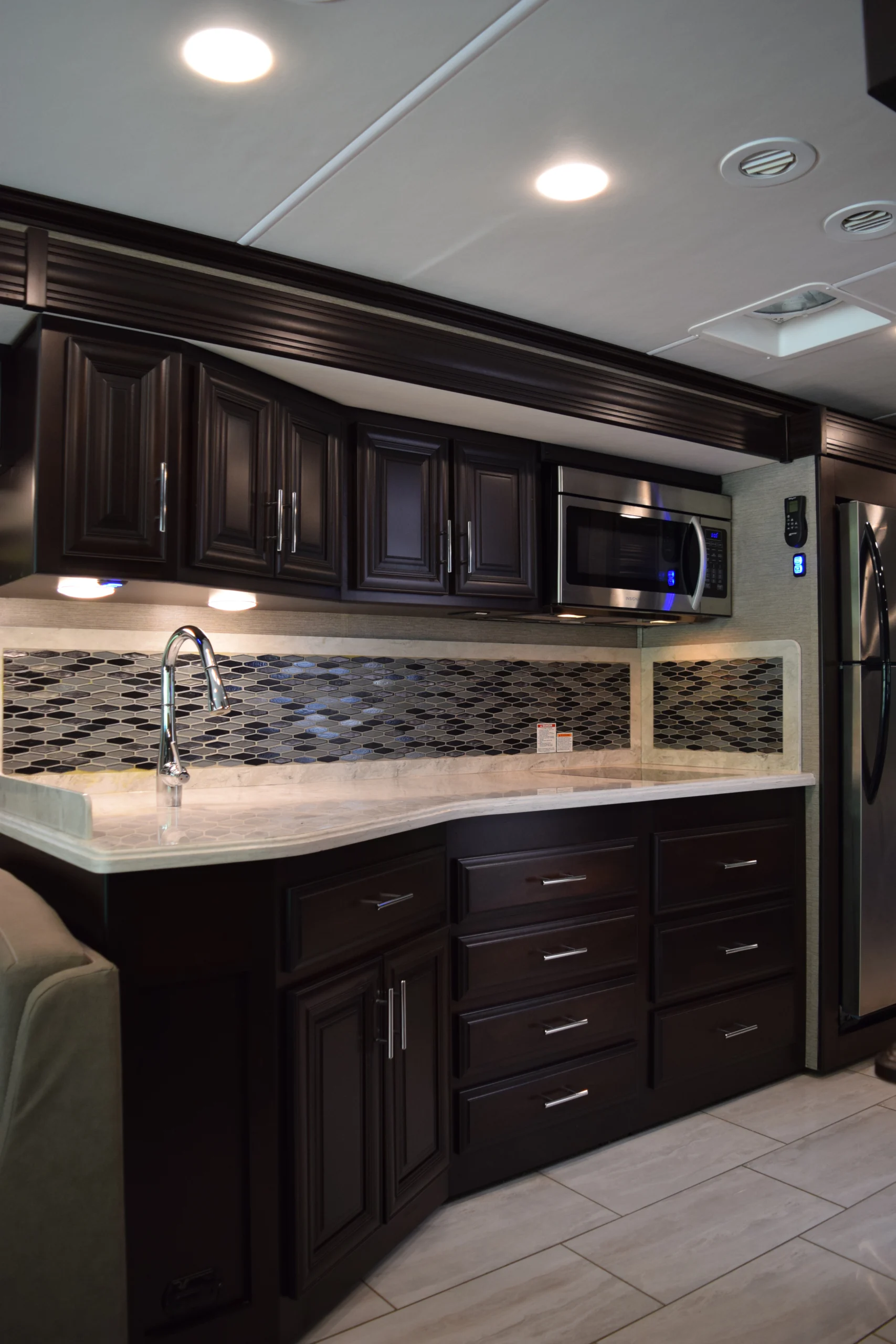 DSC_0737 Luxurious Motorcoach kitchen with dark wood cabinets, modern backsplash, stainless steel appliances, and polished countertops.