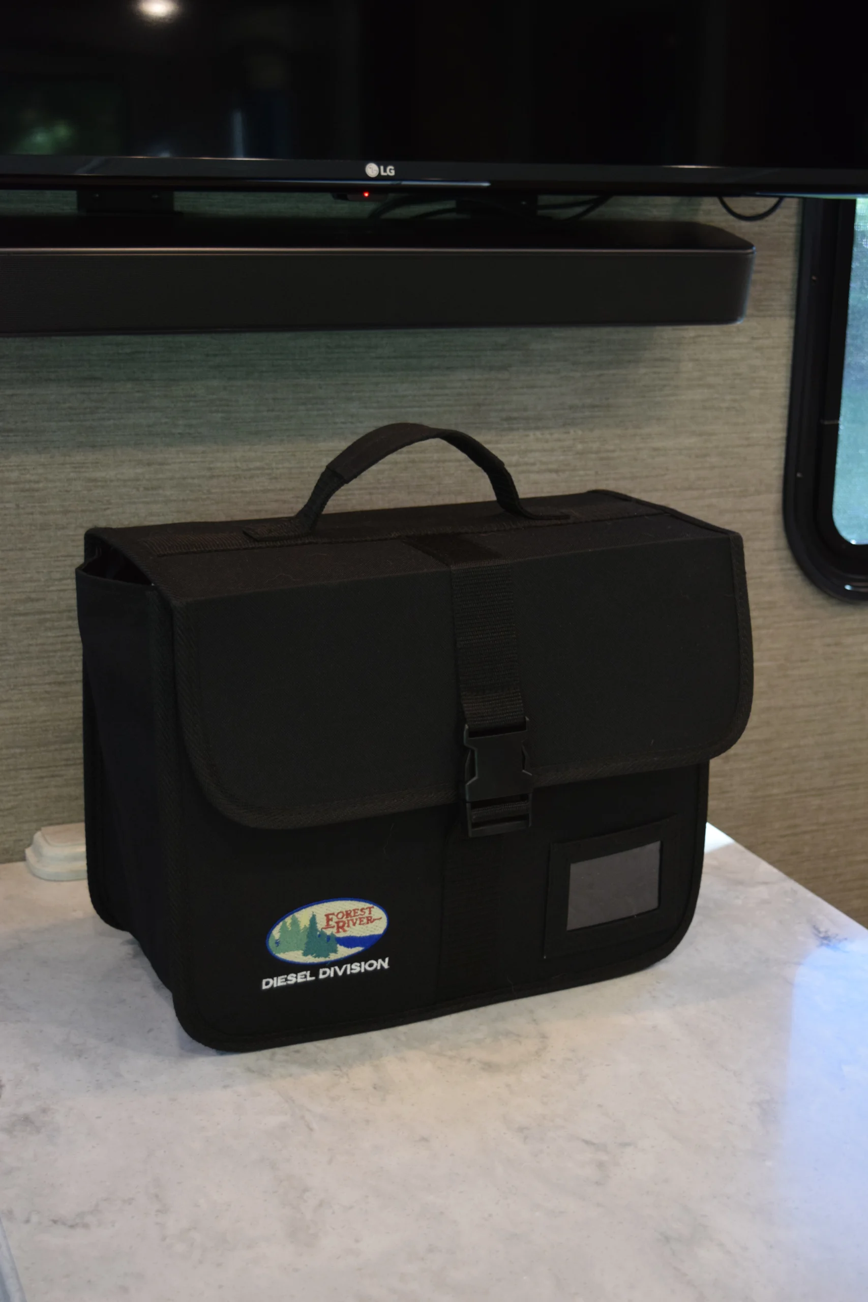 DSC_0738 Black travel bag with a handle and buckle, labeled "Diesel Division," on a table in an RV interior, TV above.