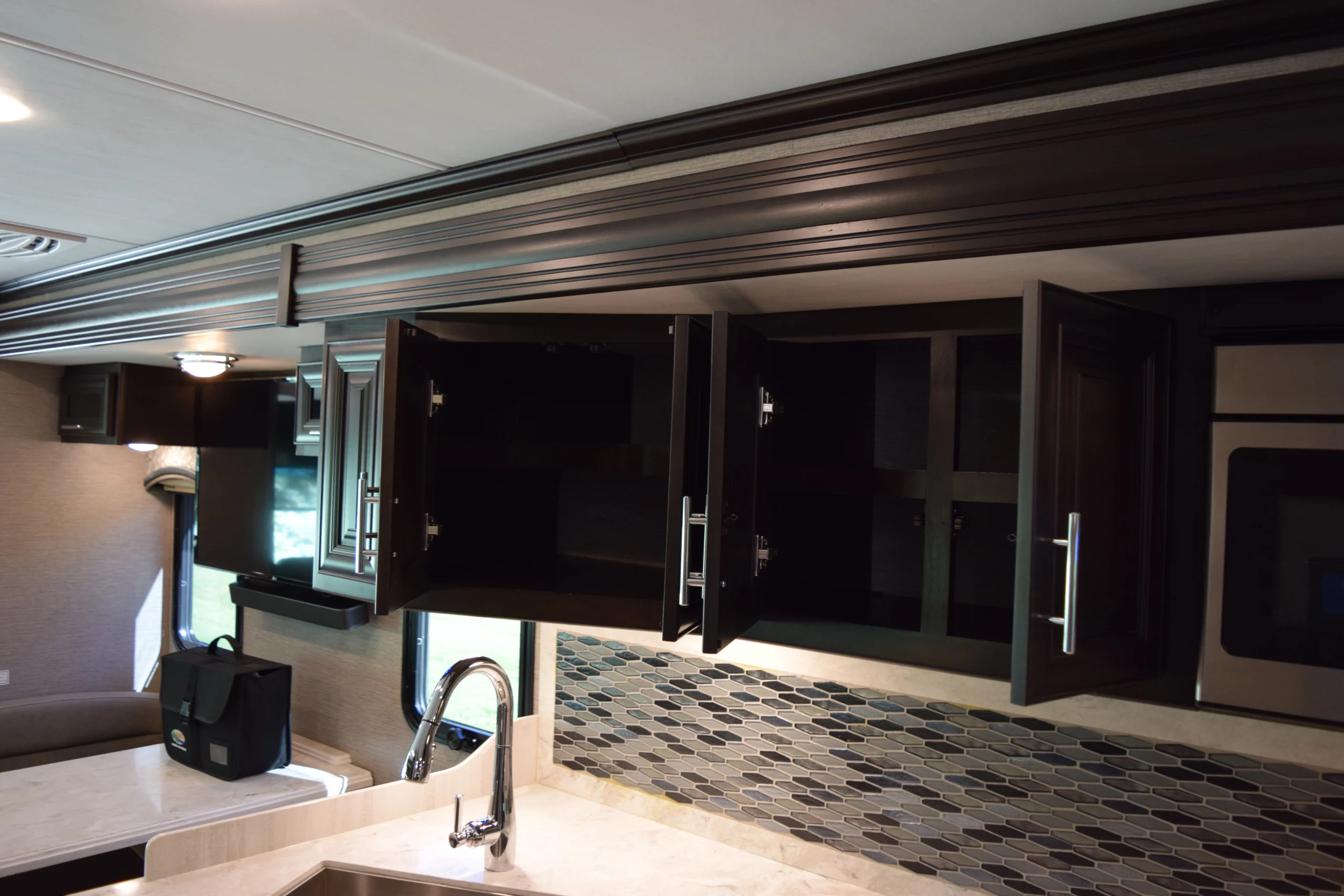 DSC_0740 Modern Motorcoach and RVs kitchen with dark wood cabinets, open doors, a sleek faucet, tiled backsplash, and natural light streaming in.