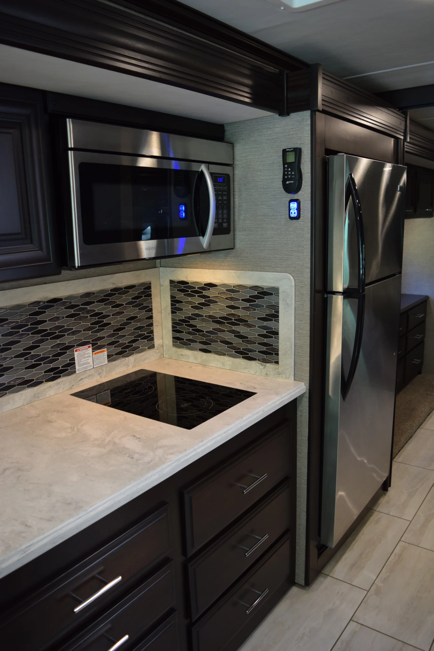 DSC_0742 Luxury motorcoach kitchen with stainless steel fridge, microwave, induction cooktop, and modern tile backsplash.
