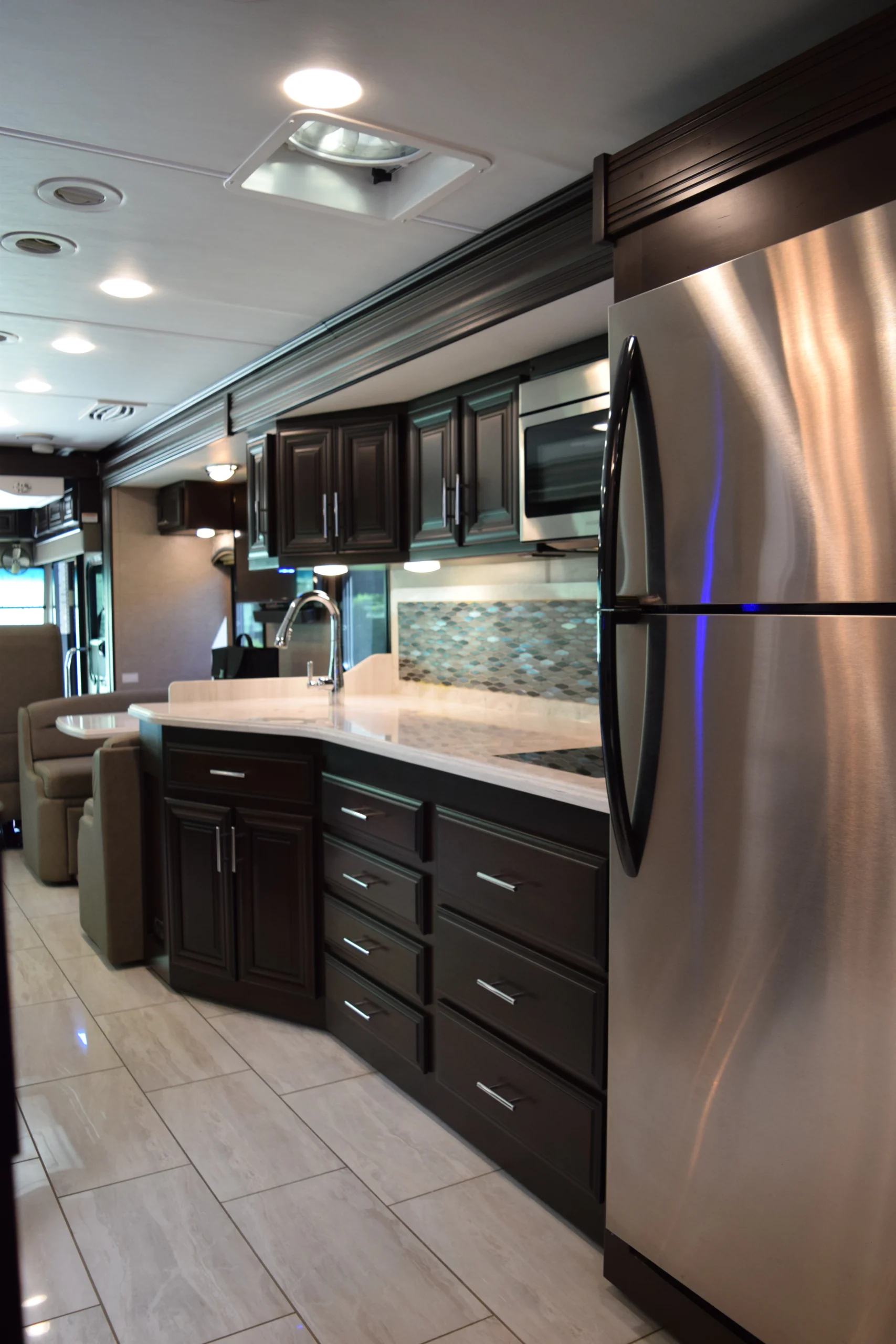 DSC_0743 Luxurious Motorcoach interior featuring a modern kitchen with dark wood cabinets, stainless steel appliances, and sleek countertops.
